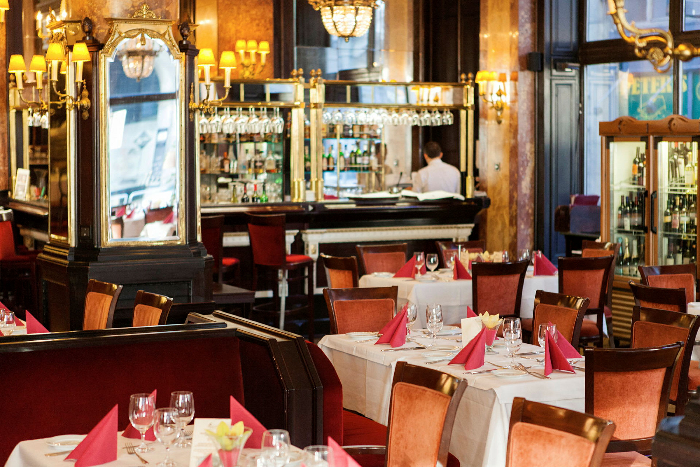 Restaurantinteriør med dekkede bord, røde servietter og glass, samt en bar i bakgrunnen. (AI-generert tekst)