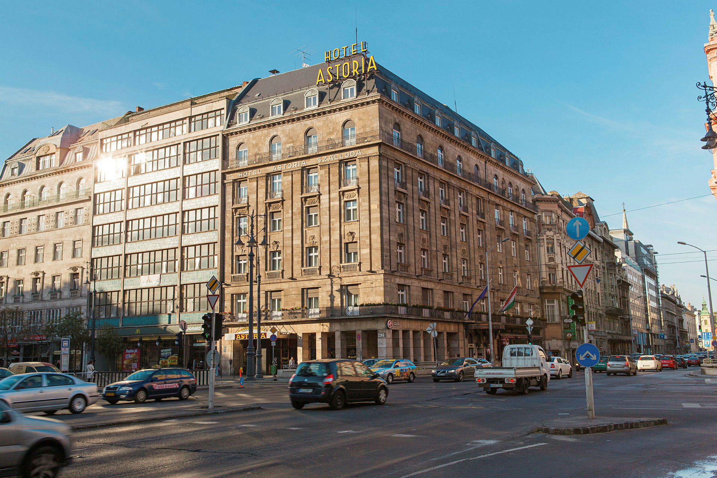 Et stort hotell i en historisk bygning med skiltet "Hotel Astoria" synlig på taket. Foran bygningen er et veikryss med trafikk. (AI-generert tekst)