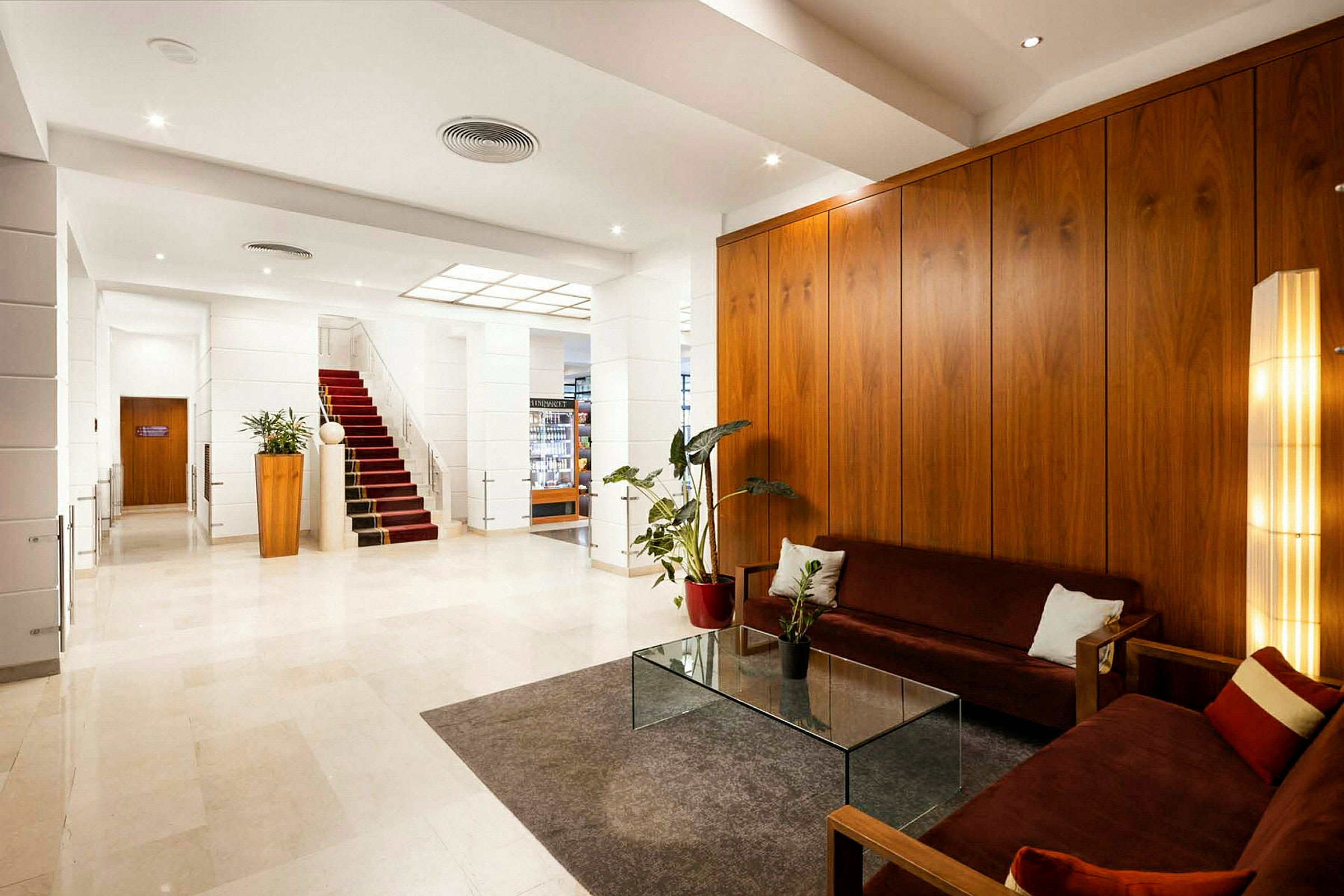 Et moderne hotellobbyområde med røde sofaer, moderne glassbord og veggpaneler i tre. (AI-generert tekst)