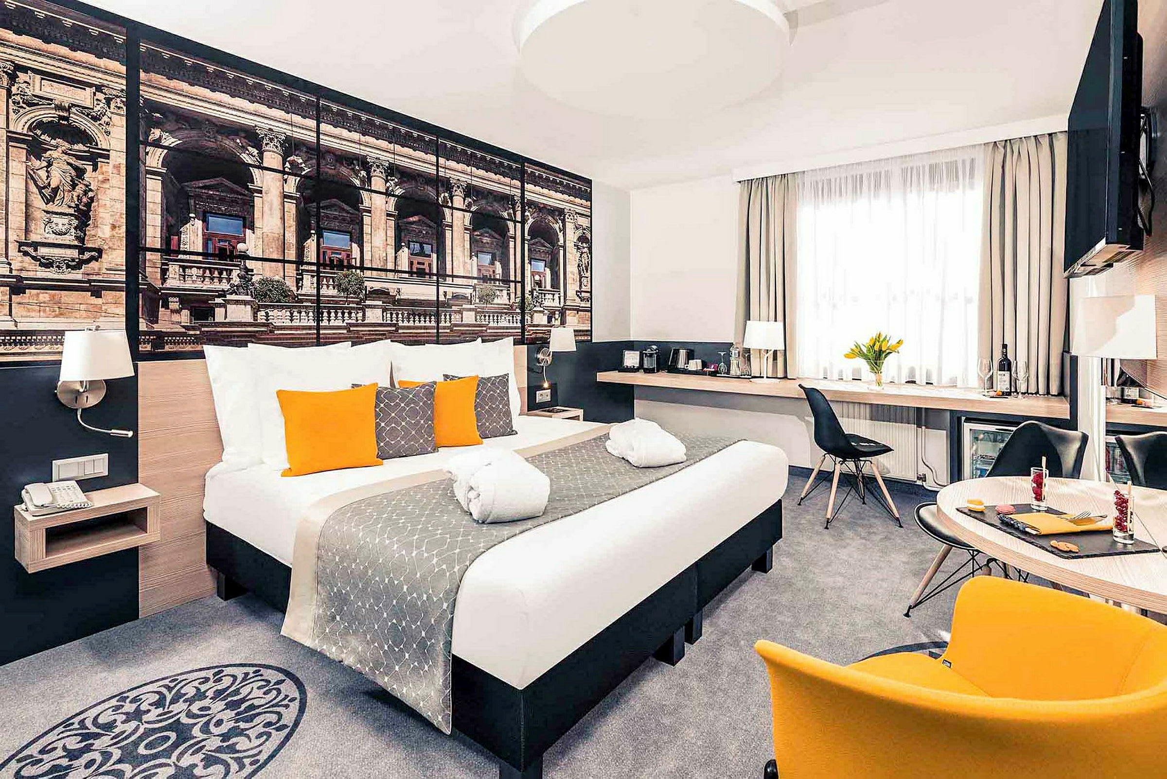 Moderne hotellrom med dobbeltseng, dekorative puter og et stort veggbilde av arkitektur. (AI-generert tekst)