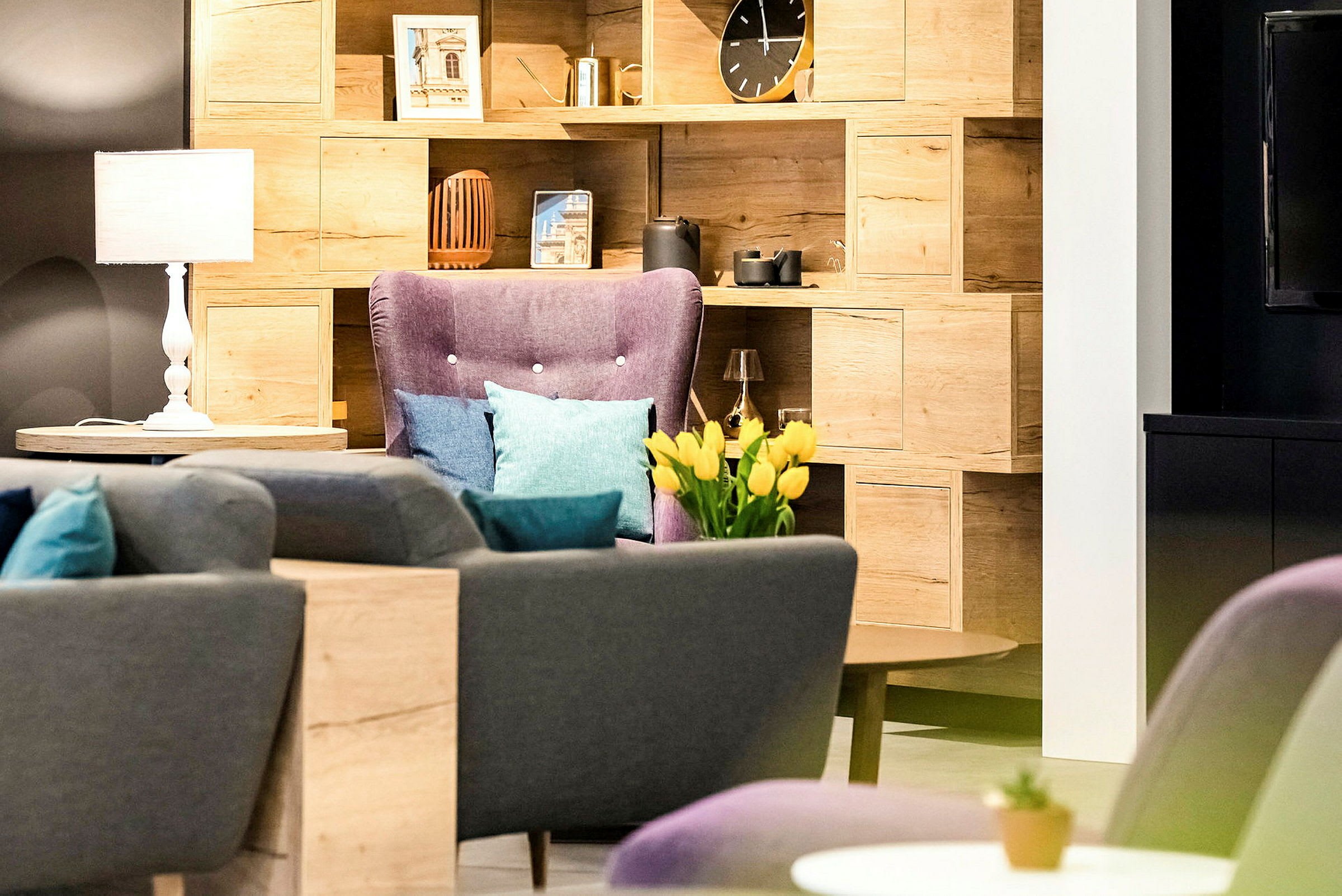 En stue med en bokhylle, lenestol, sofaer og dekorative gjenstander, inkludert en vase med gule tulipaner. (AI-generert tekst)
