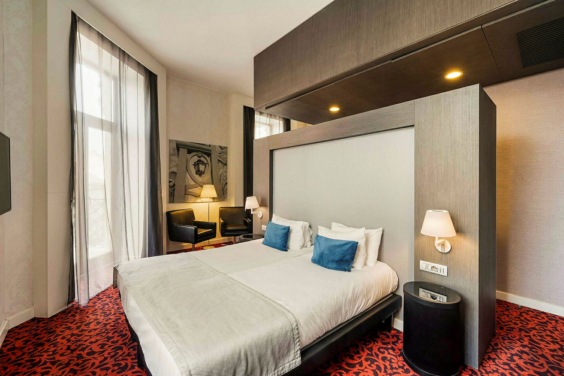 Et moderne hotellrom med dobbeltseng, nattbord og sittegruppe med stoler. (AI-generert tekst)