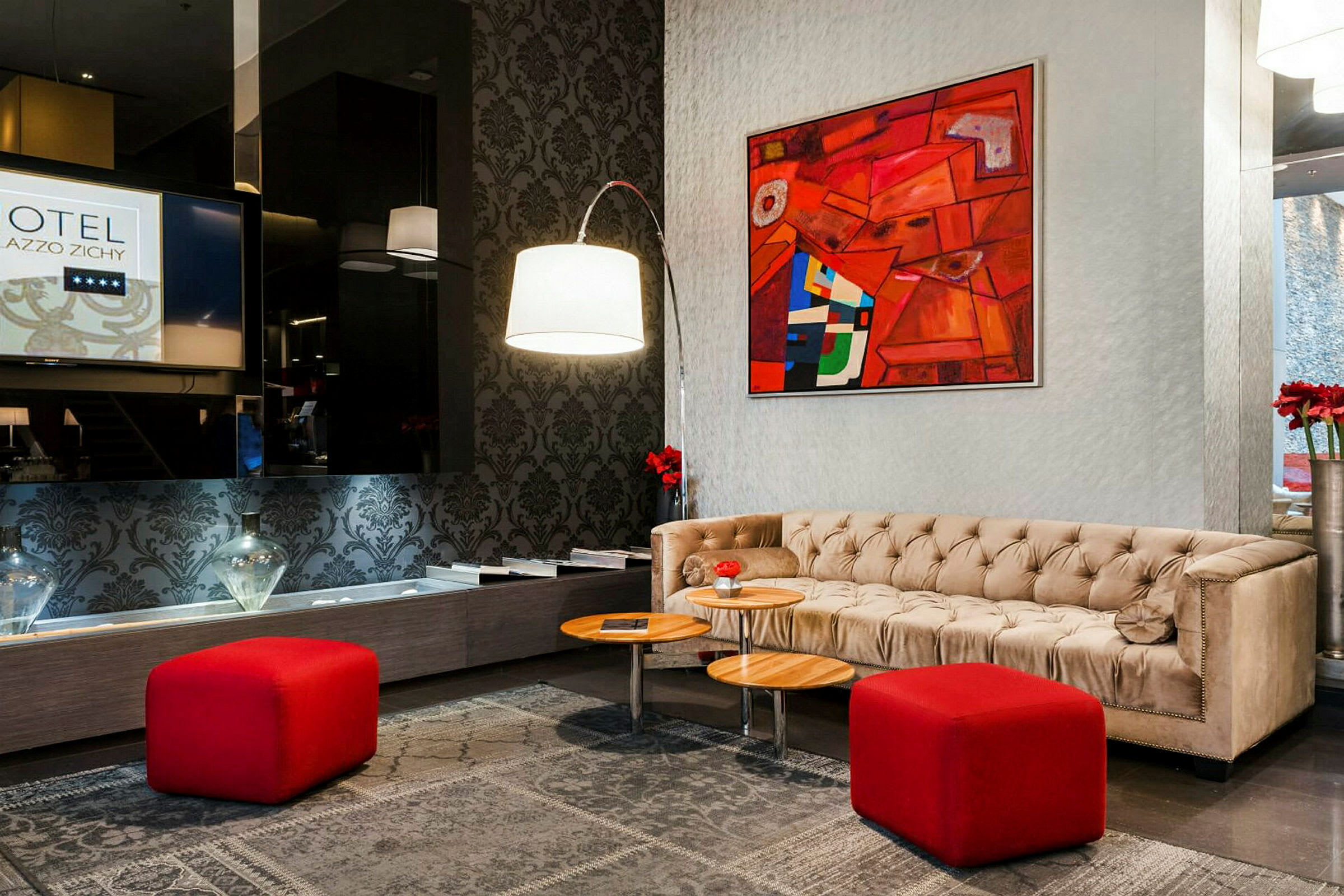 Et hotellobbyområde med en beige sofa, røde krakker og et abstrakt kunstverk på veggen. (AI-generert tekst)