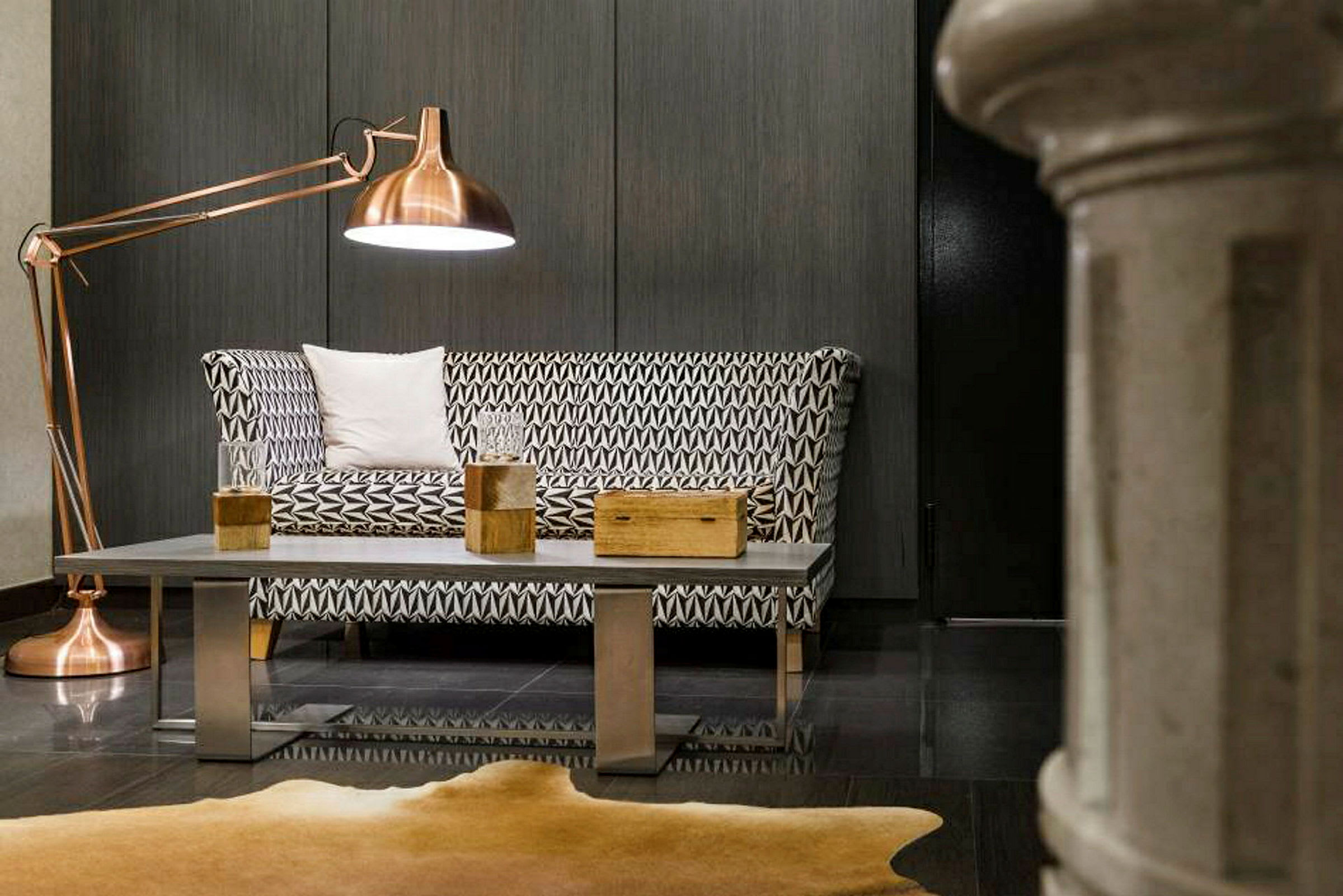 Et moderne rom med en geometrisk mønstret sofa, metallbord med tredekorasjoner og stor kobberfarget gulvlampe. (AI-generert tekst)