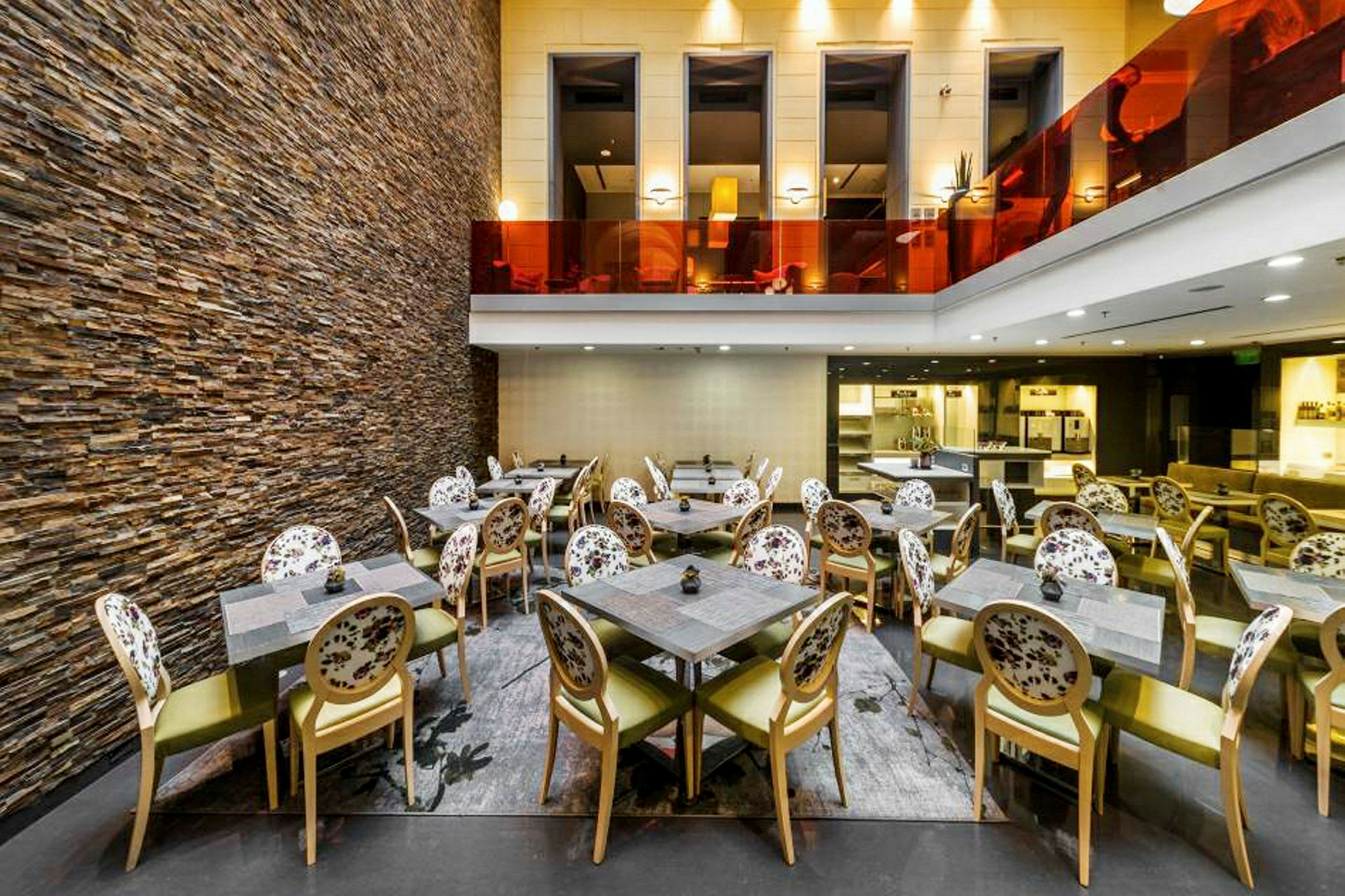 Interiør av en restaurant med stoler og bord, samt en vegg av stein. (AI-generert tekst)