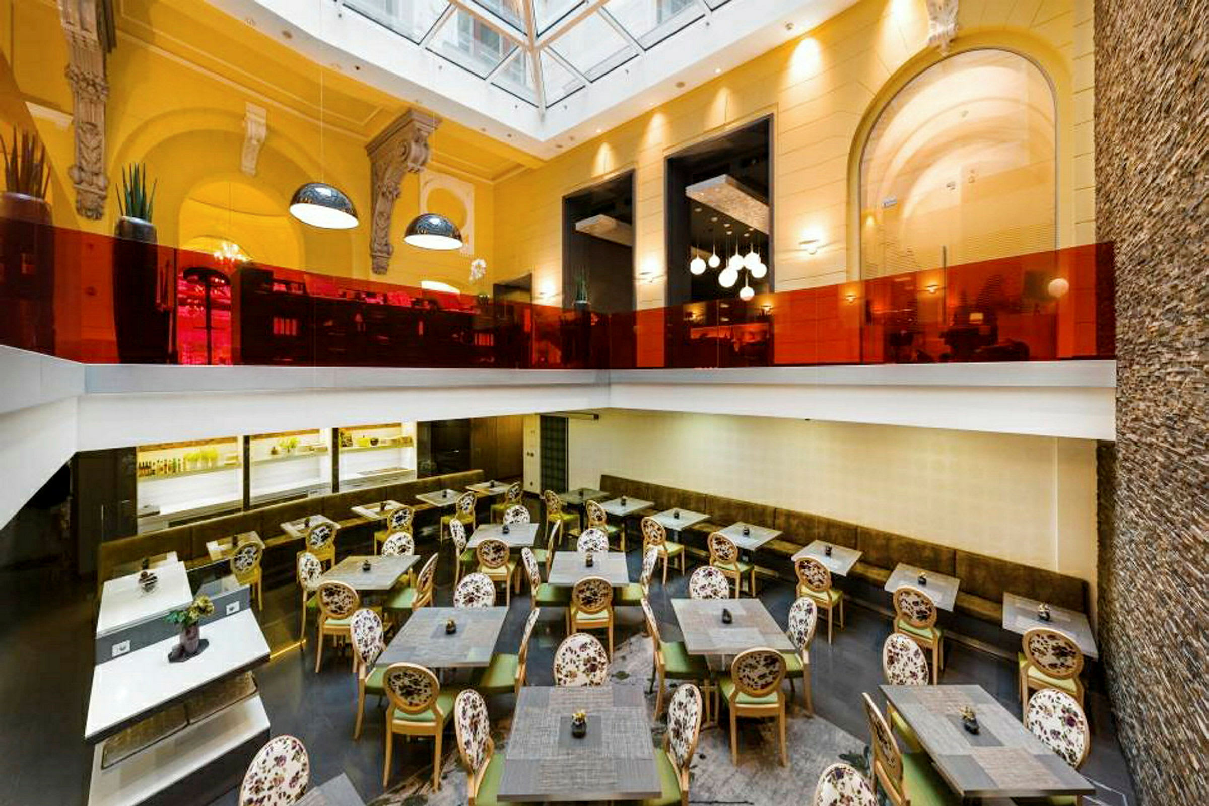 Et restaurantområde med bord, stoler og en øvre etasje innredet med forskjellige lamper og glasdetaljer. (AI-generert tekst)