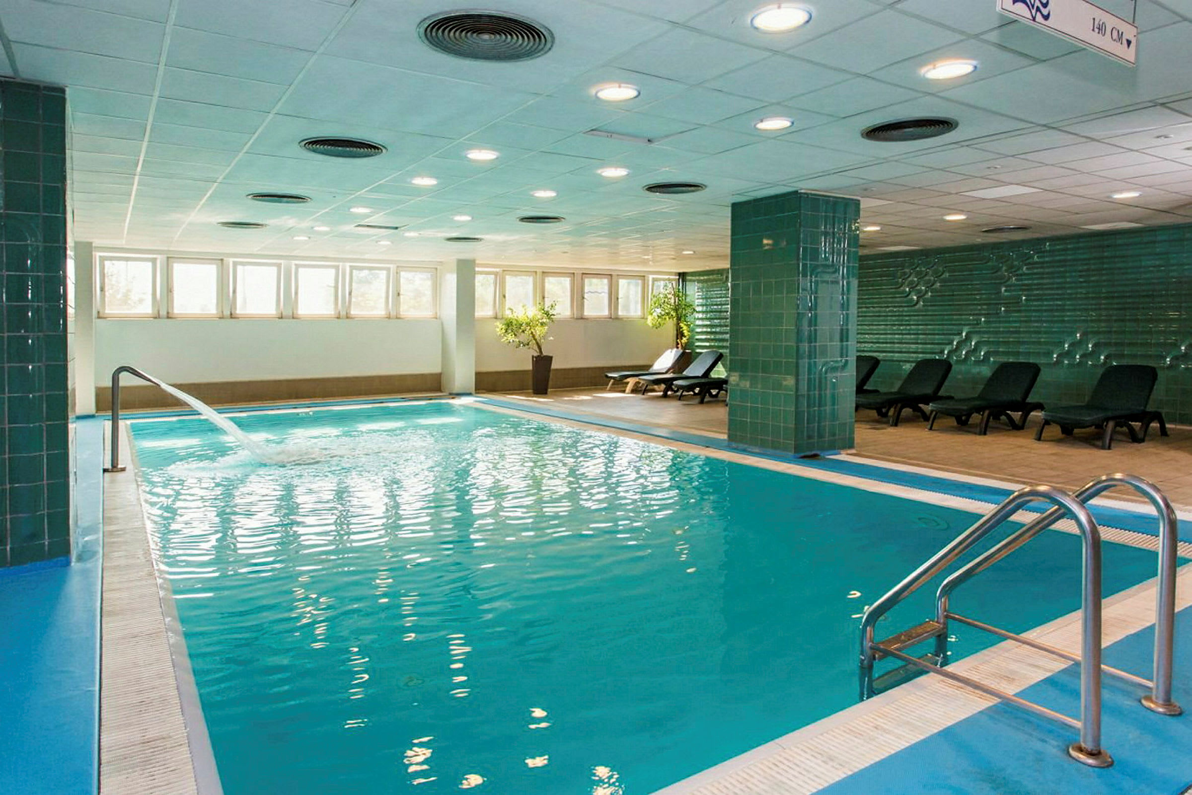 Innendørsbasseng med solsenger på siden og en fontene som renner inn i vannet. (AI-generert tekst)