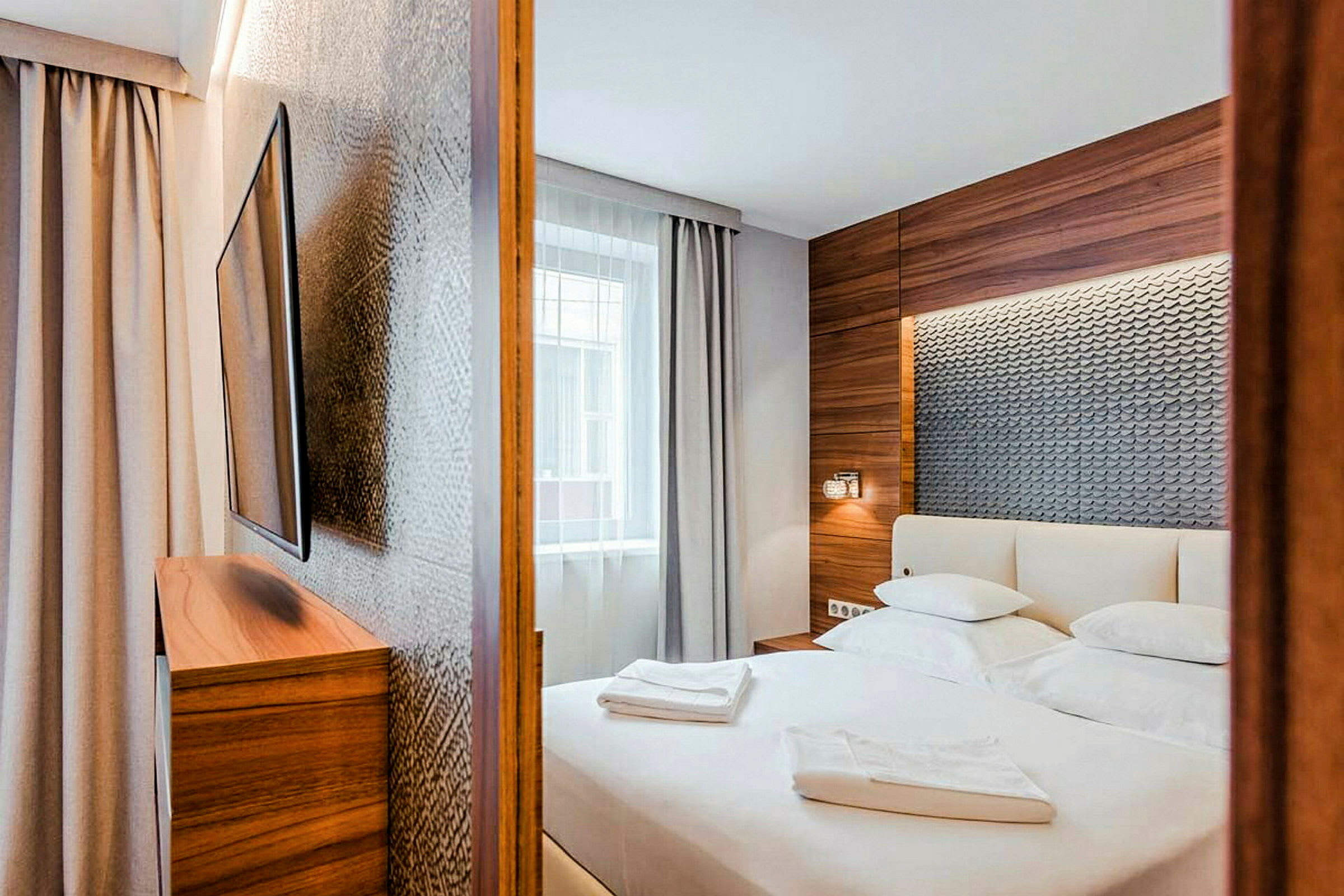 Et moderne hotellrom med en stor seng, dekorert med trepaneler og teksturert vegg bak sengegavlen. (AI-generert tekst)