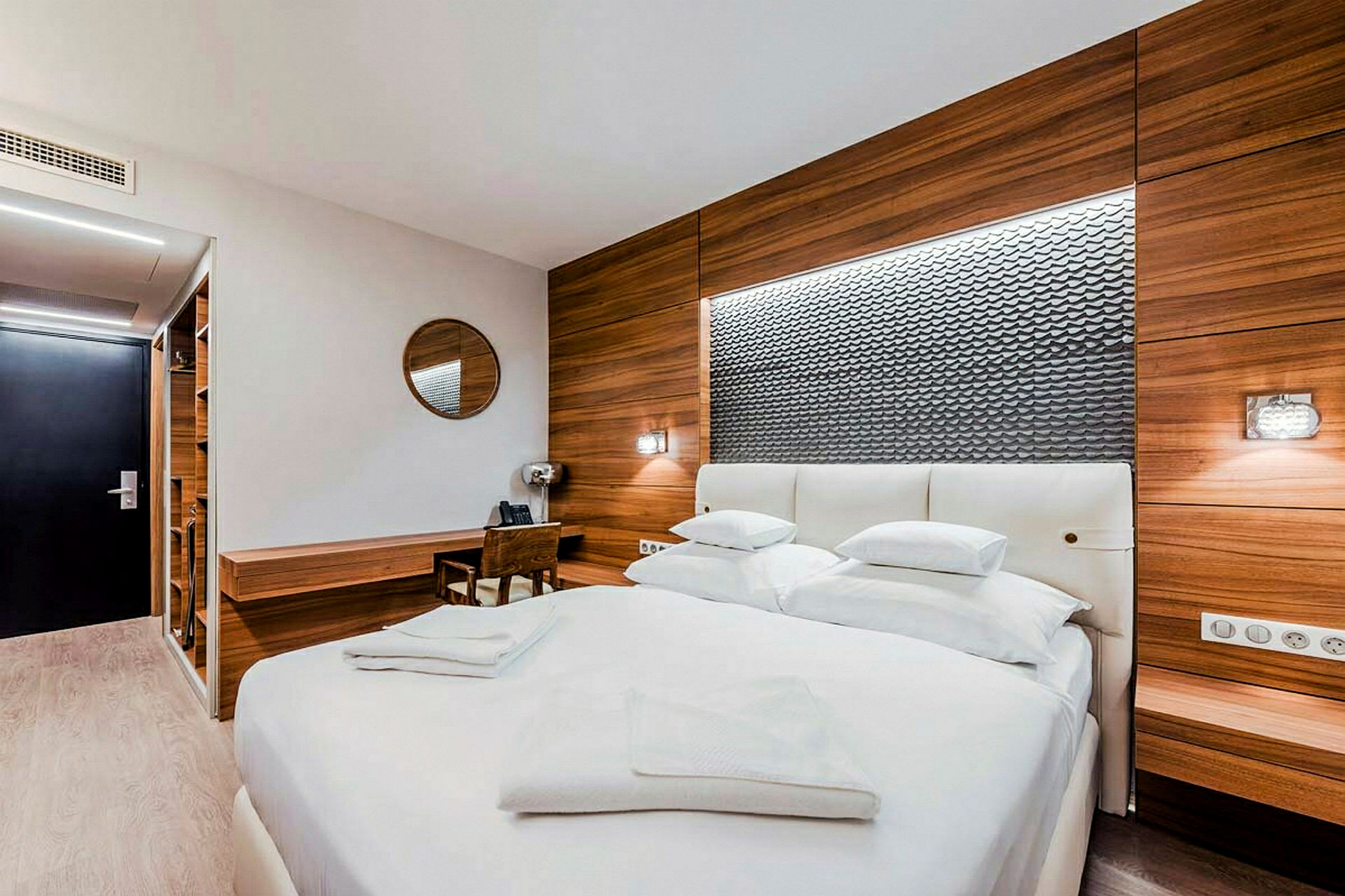 Et moderne hotellrom med en stor dobbeltseng, treverk på veggene og en skrivebordsflate. (AI-generert tekst)