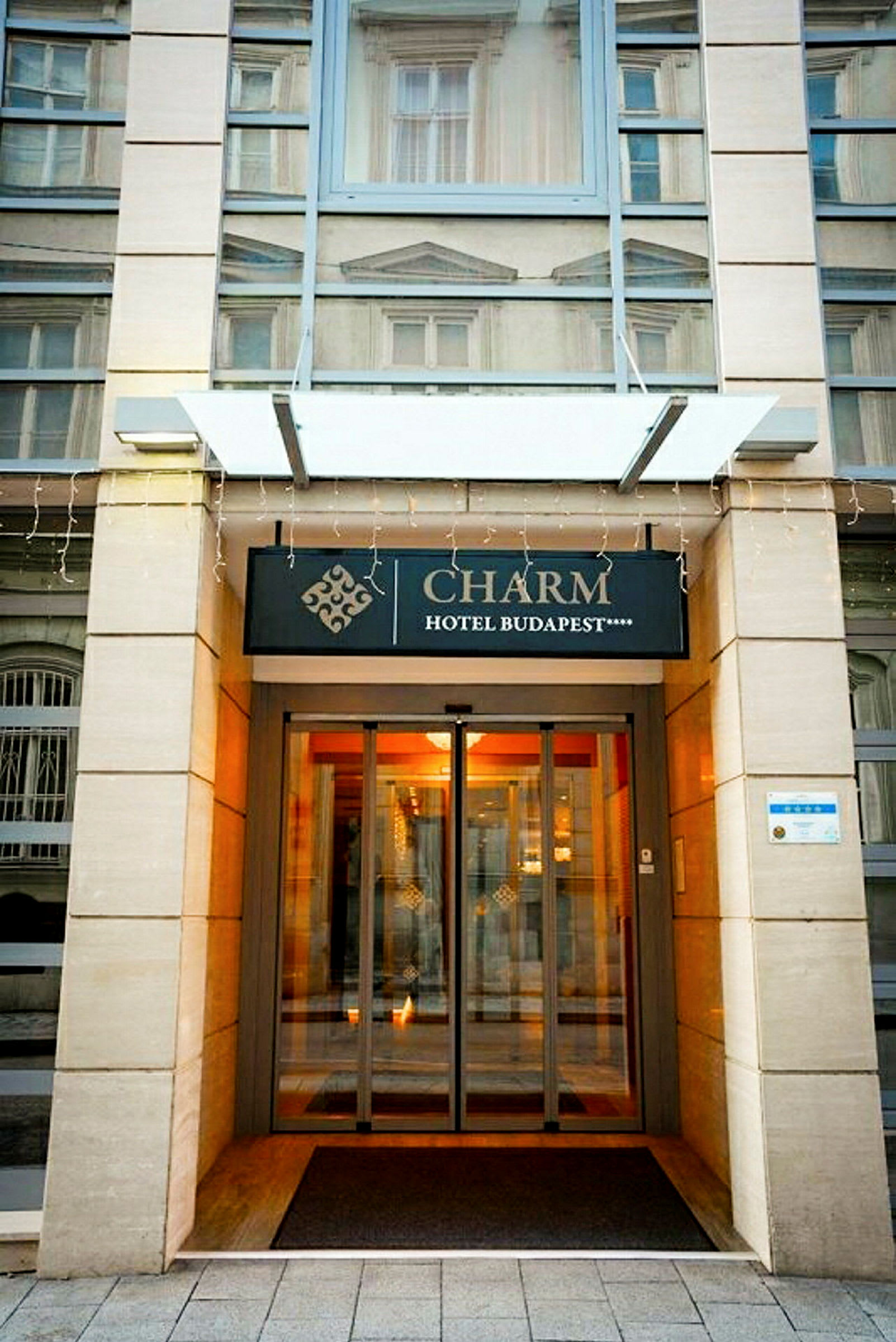 Inngangen til Charm Hotel Budapest med skilt og glassdører. (AI-generert tekst)
