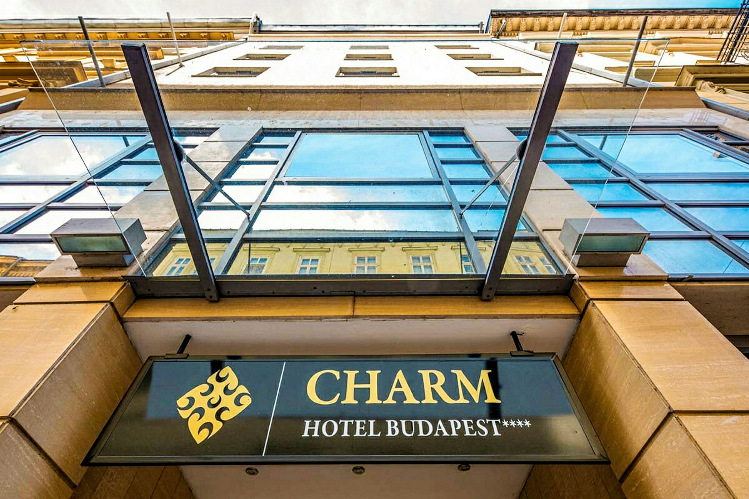 Fasadebilde av en bygning med et skilt som viser navnet "CHARM Hotel Budapest****". (AI-generert tekst)