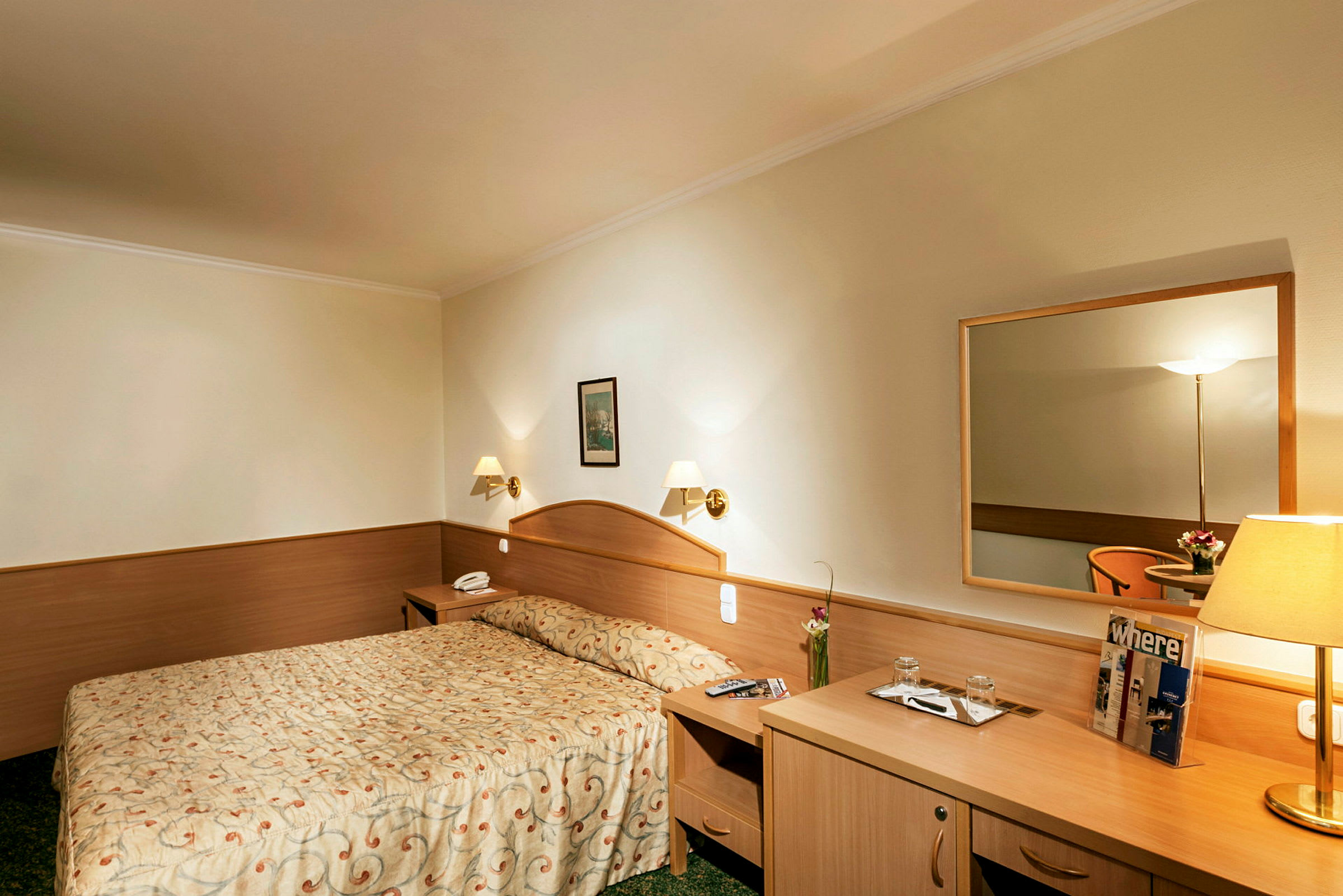 Hotellrom med dobbeltseng, nattbord, speil og skrivebord. (AI-generert tekst)