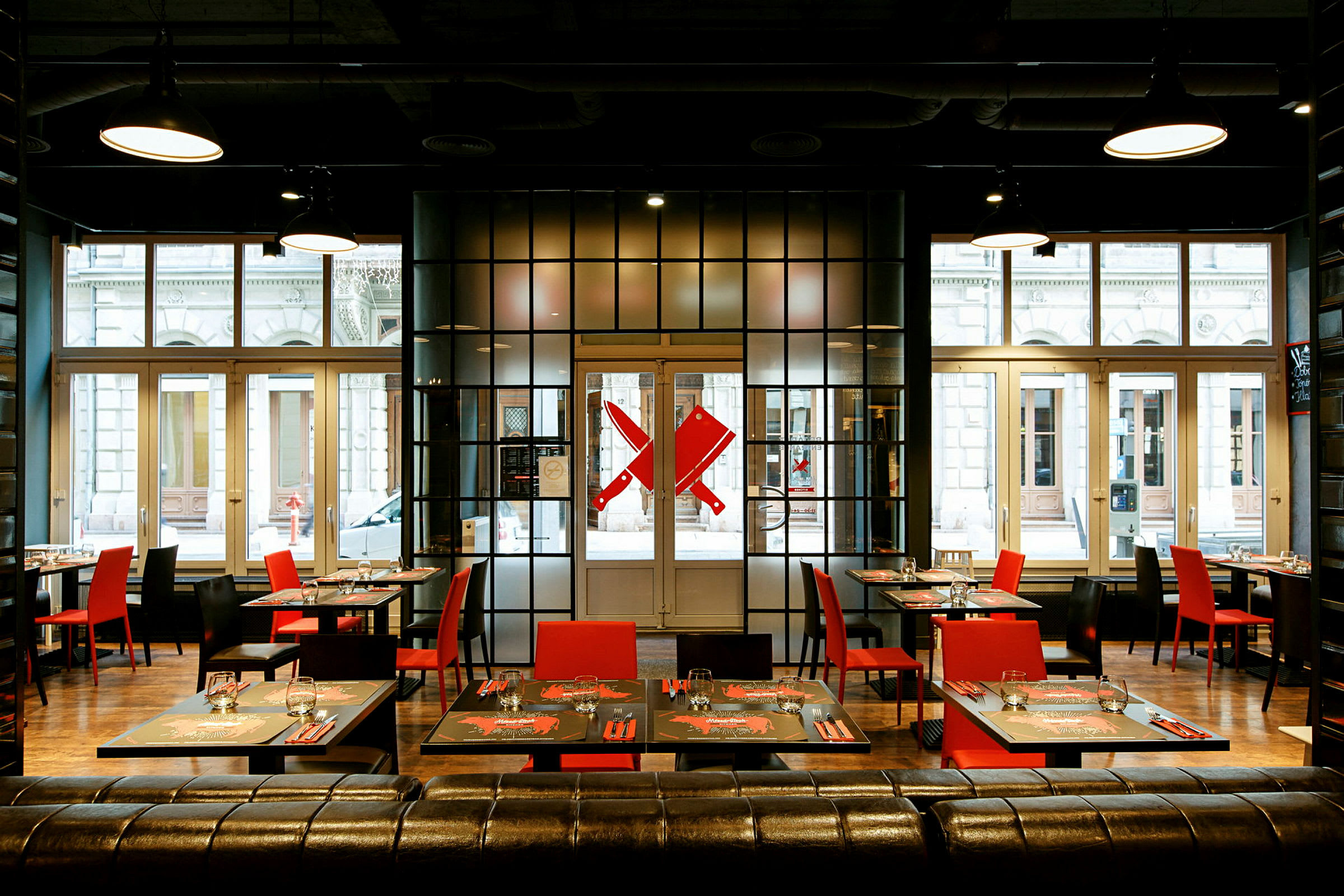 Moderne restaurant med røde og svarte stoler samt dekkede bord foran store vinduer. (AI-generert tekst)