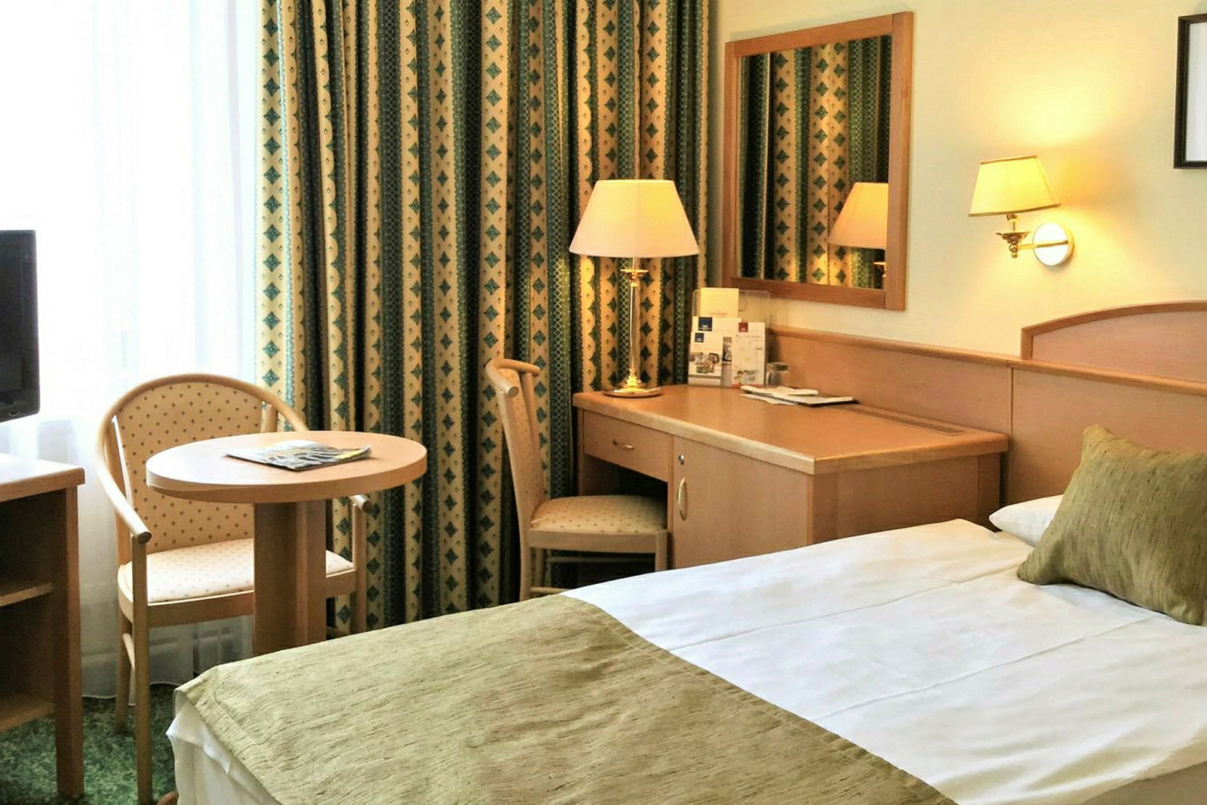 Hotellrom med seng, skrivebord og sitteplass ved et lite bord. (AI-generert tekst)