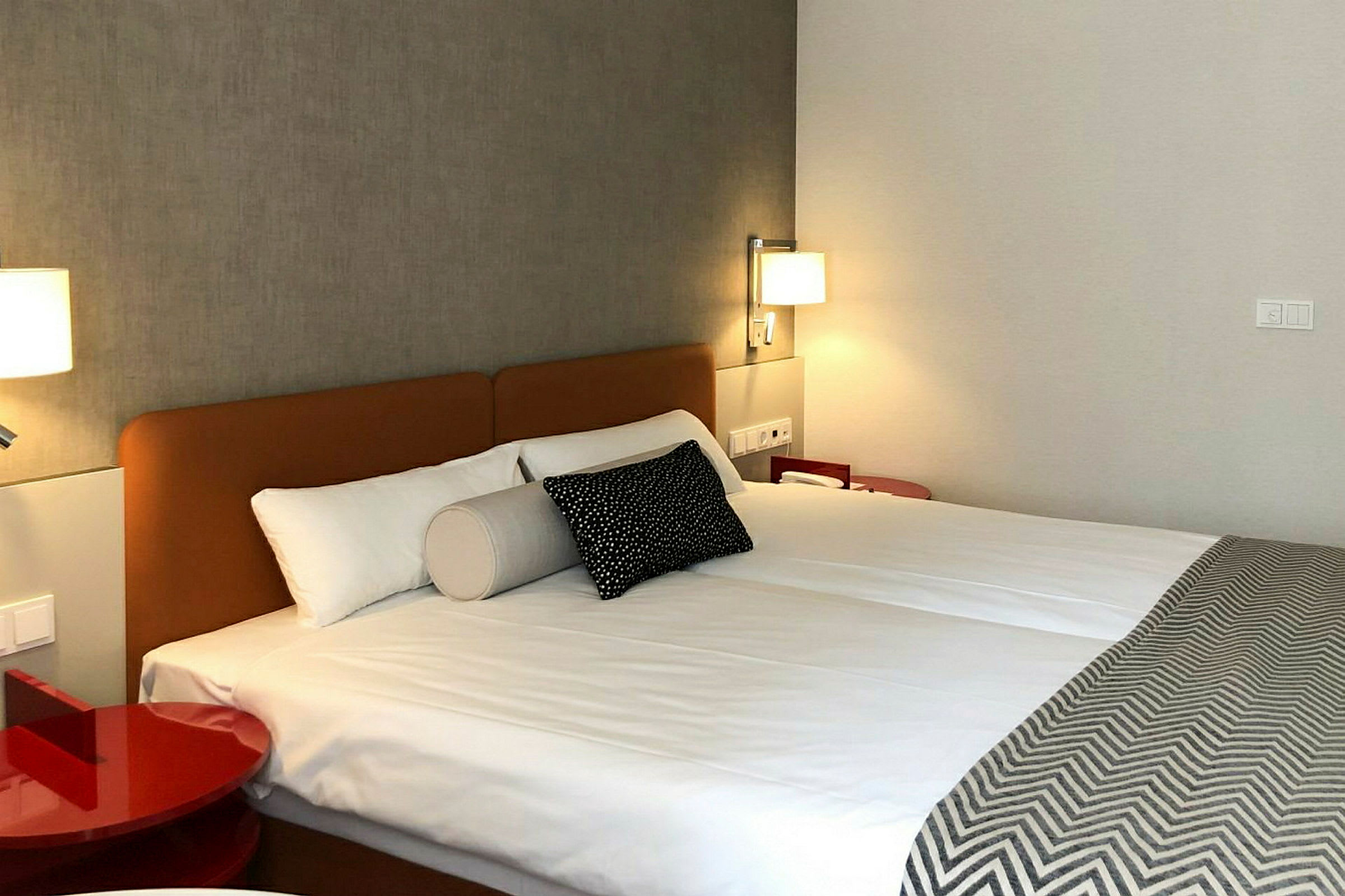Et hotellrom med en dobbeltseng, opplyst med vegglamper. (AI-generert tekst)