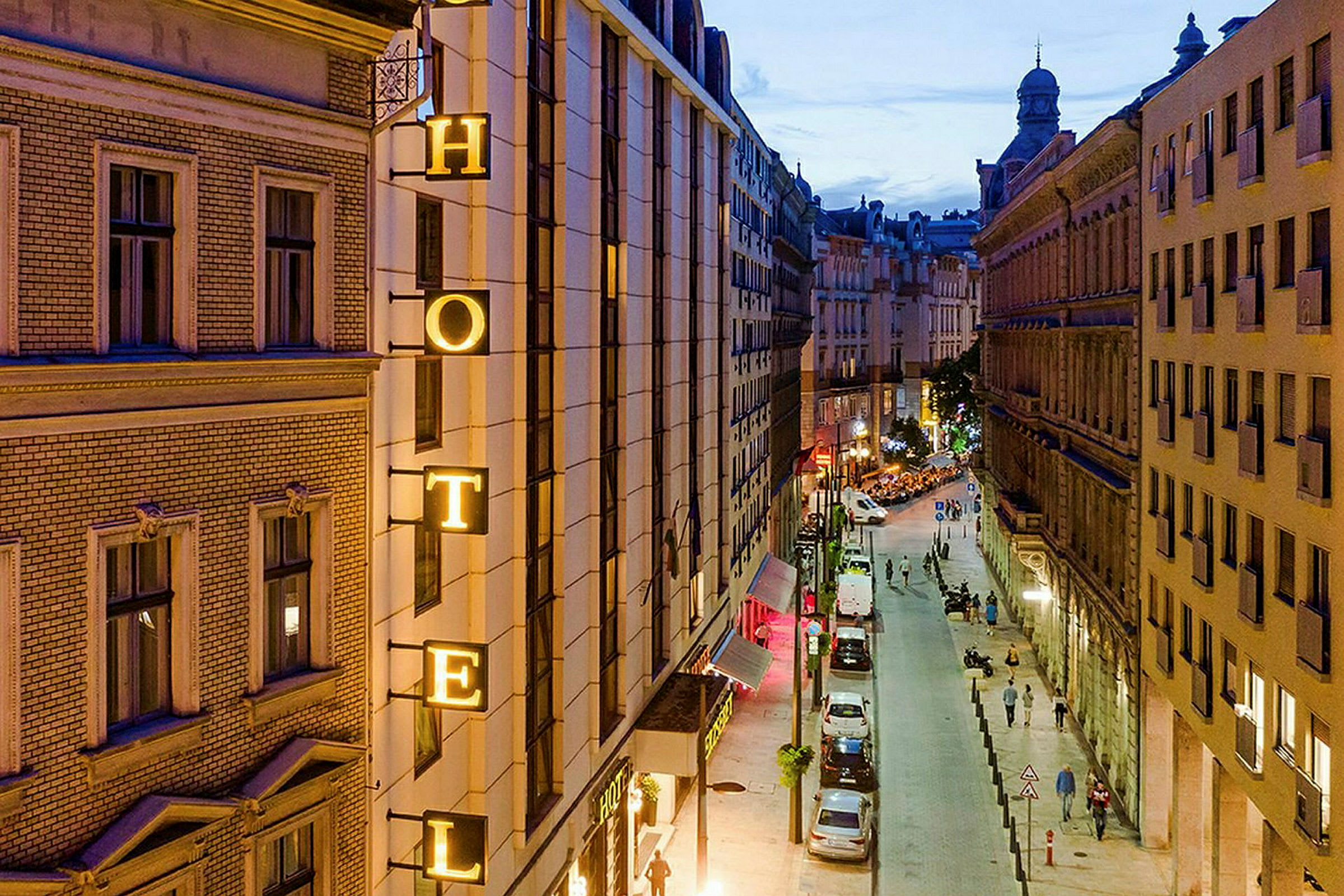 Bilde av en bygate om kvelden med et hotellskilt på en bygning. (AI-generert tekst)