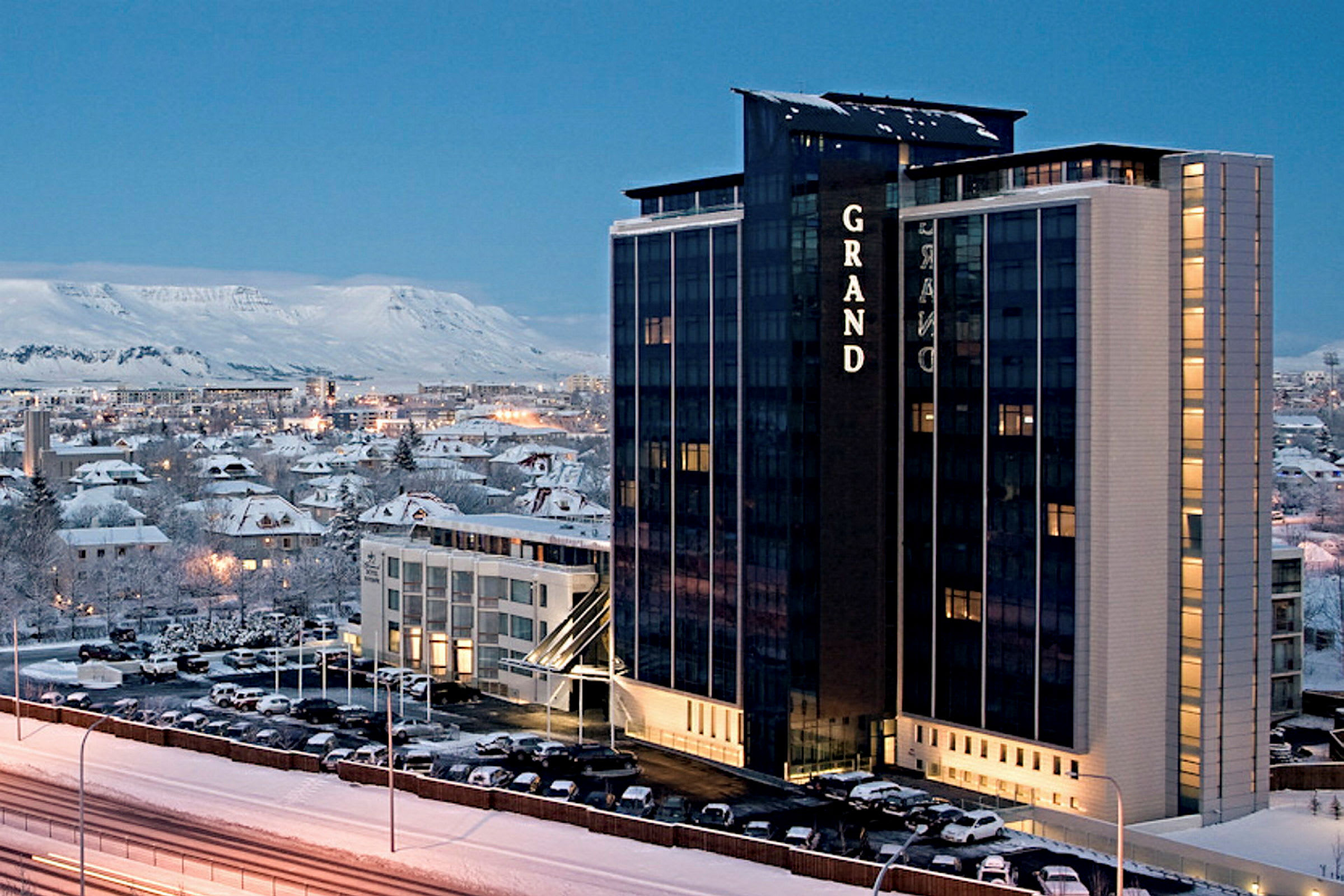 Et høyhus hotell i vinterlig miljø med en by og fjell i bakgrunnen. (AI-generert tekst)