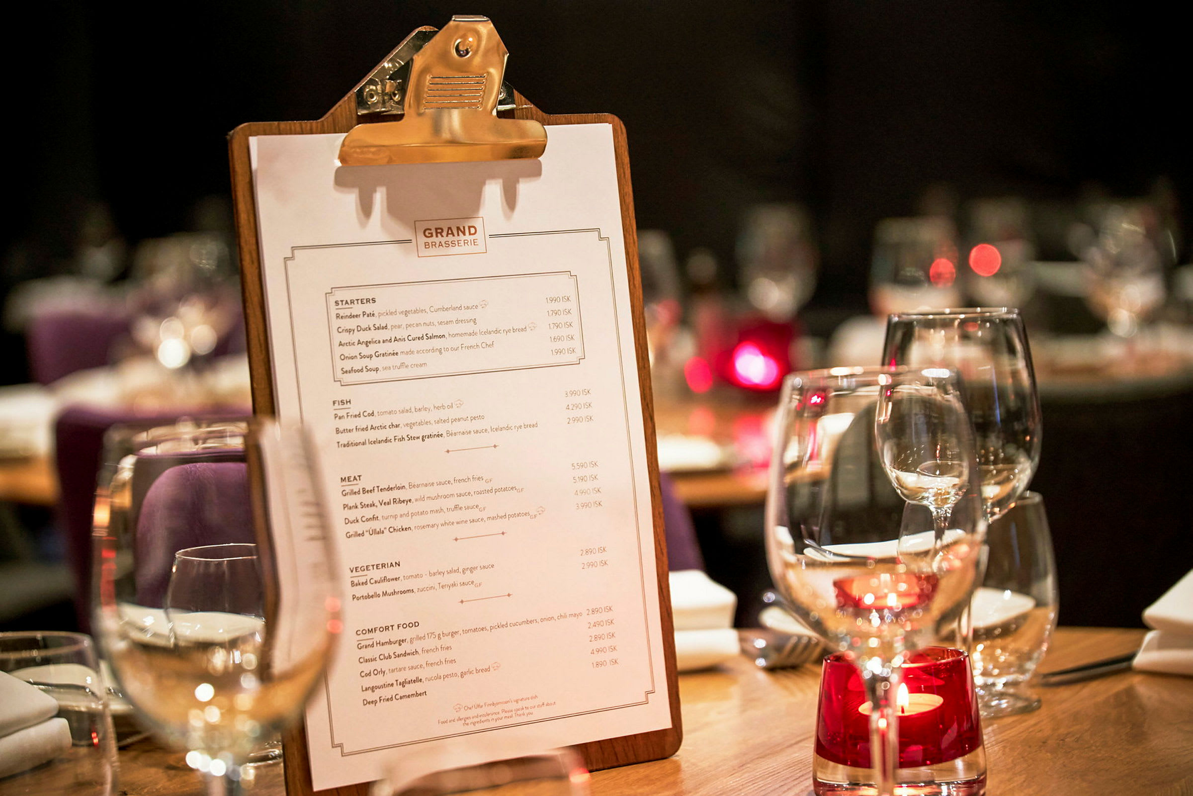 Et bord på en restaurant med en meny på en clipboard og glass med borddekorasjon. (AI-generert tekst)