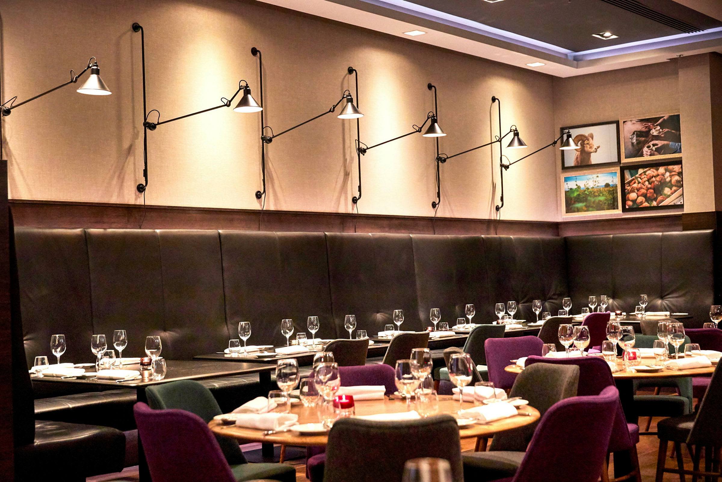 En moderne restaurant med dekkede bord og stoler, samt veggbelysning på en polstret vegg. (AI-generert tekst)
