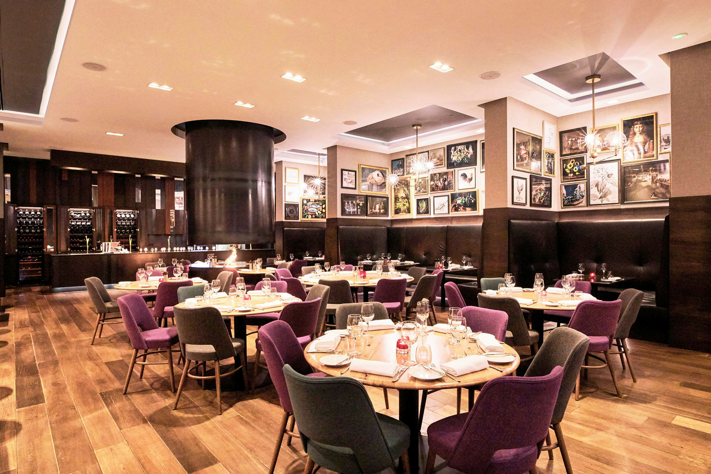 Et velopplyst restaurantinteriør med dekkede bord, fargerike stoler og en koselig atmosfære. (AI-generert tekst)