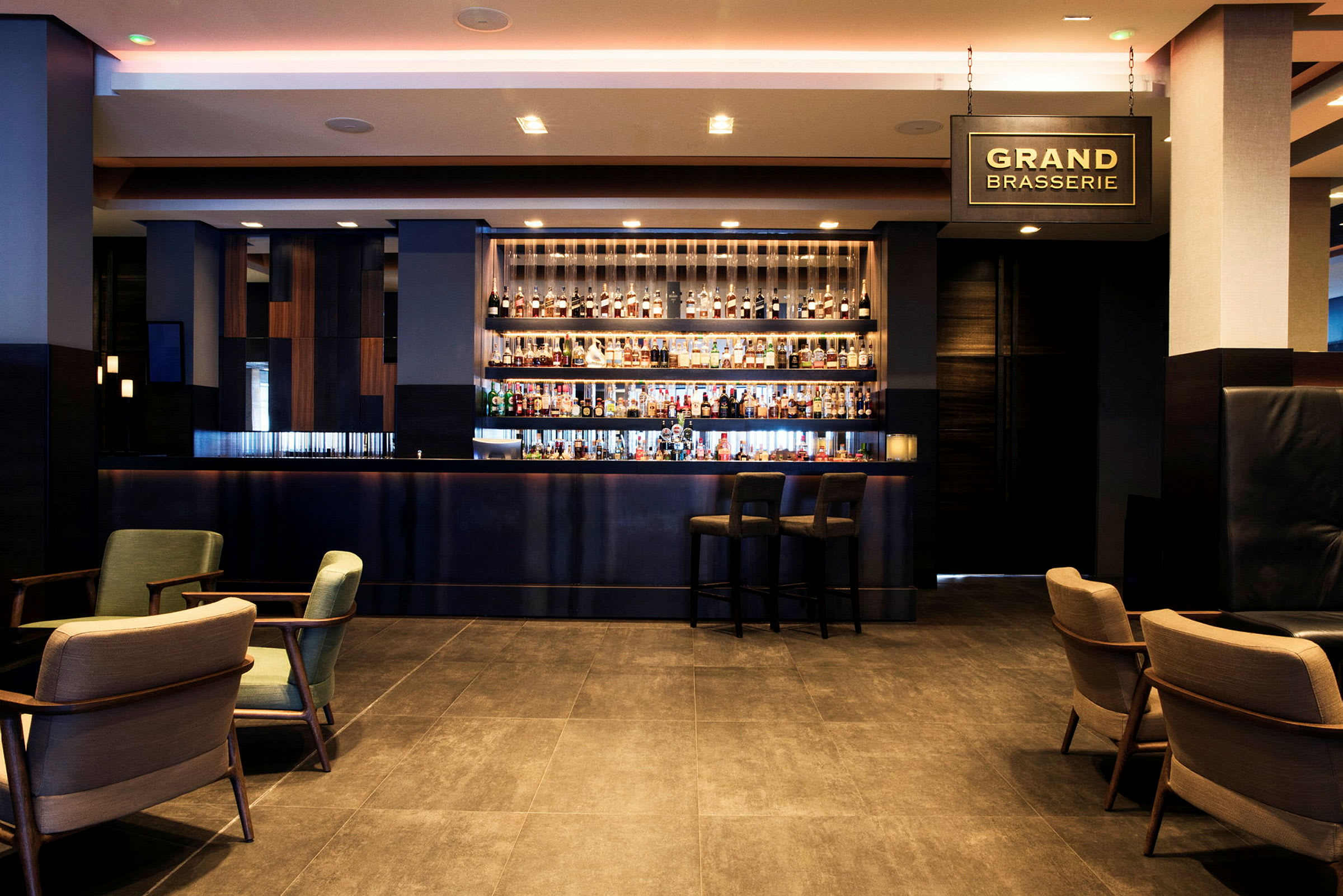 En moderne hotellbar med en opplyst bardisk og ulike flasker sprit synlige på hyllene bak. (AI-generert tekst)