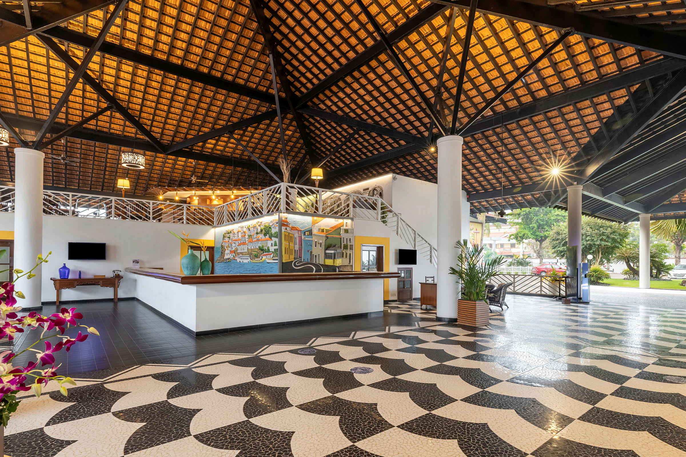 Hotellobby med en høy takstruktur av trepanel, fargerik kunst på vegger, store søyler og elegant mønstret gulv. (AI-generert tekst)