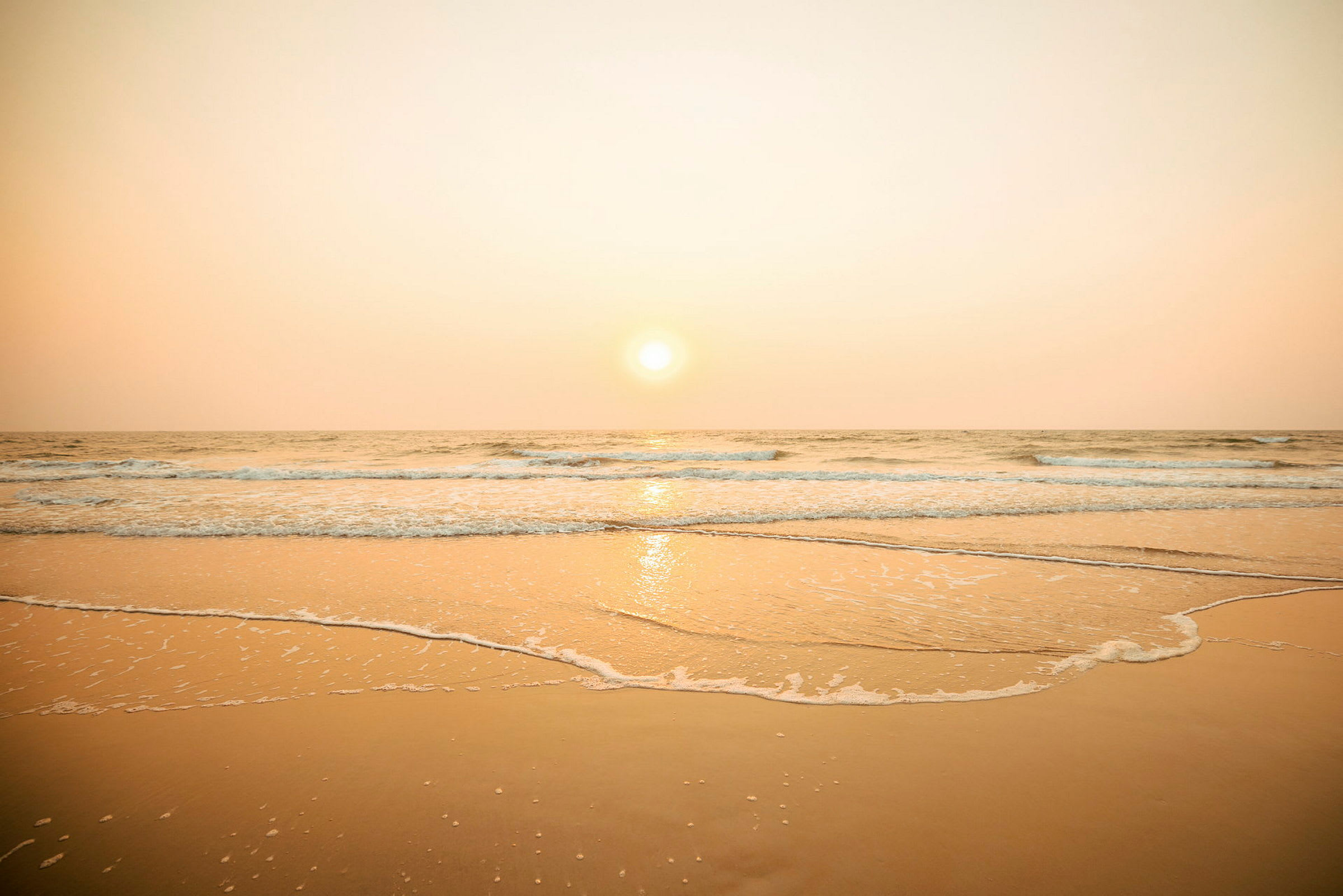 En solnedgang over havet med bølger som når en sandstrand. (AI-generert tekst)