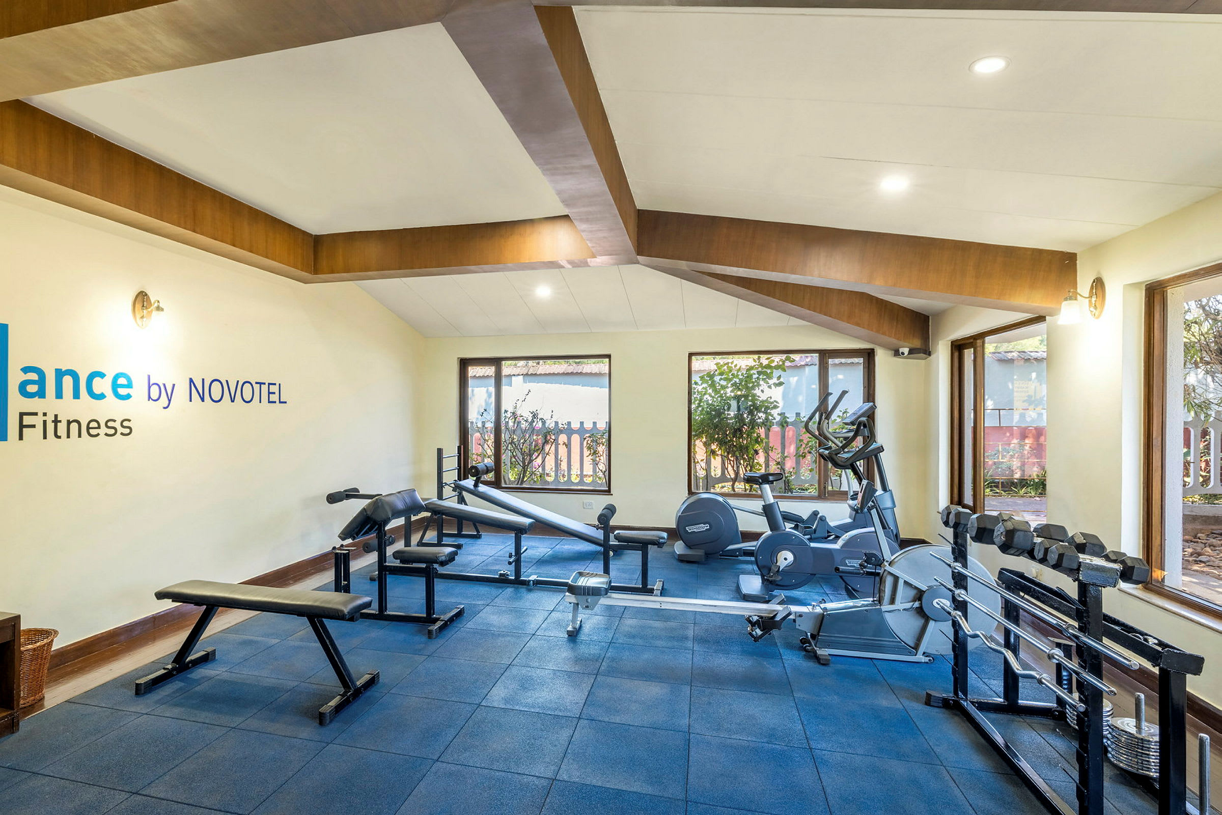 Et treningssenter med treningsutstyr, vinduer og et skilt med teksten 'Balance by NOVOTEL Fitness'. (AI-generert tekst)