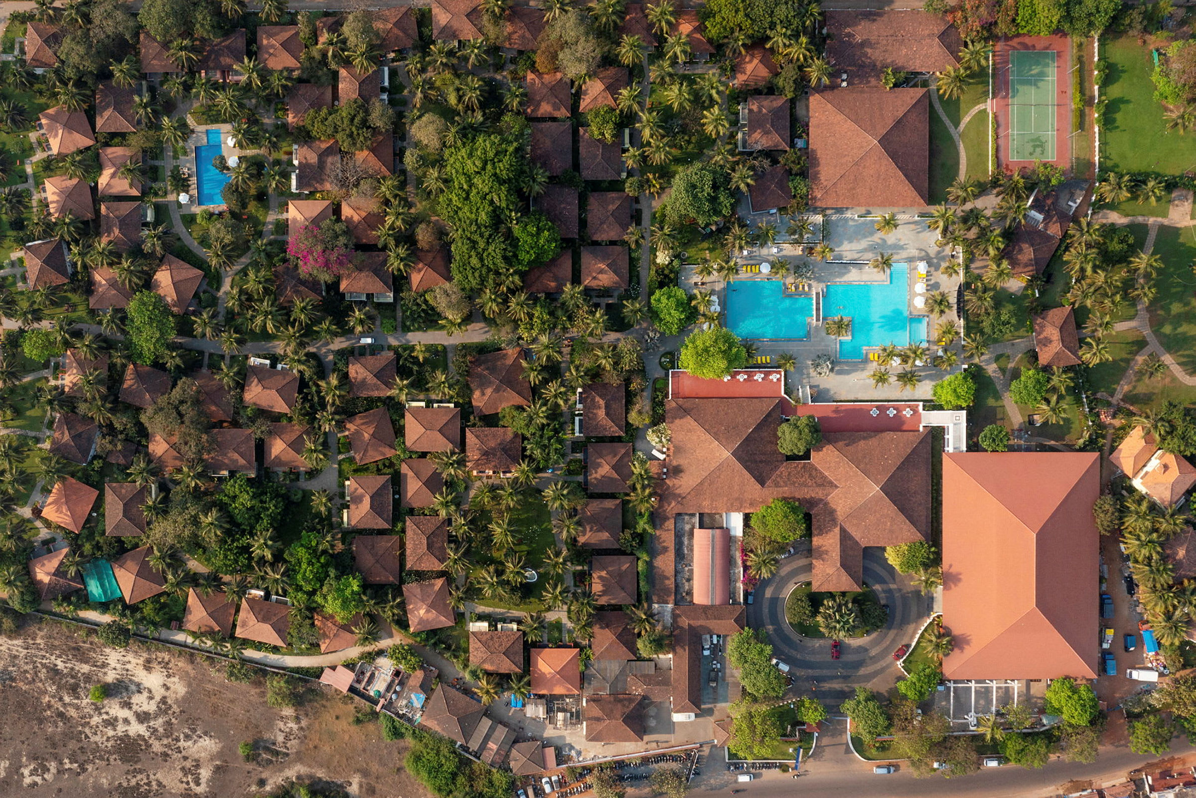 Et flyfoto som viser en resort med terrakottatak, grøntområder, bassenger og tennisbaner. (AI-generert tekst)