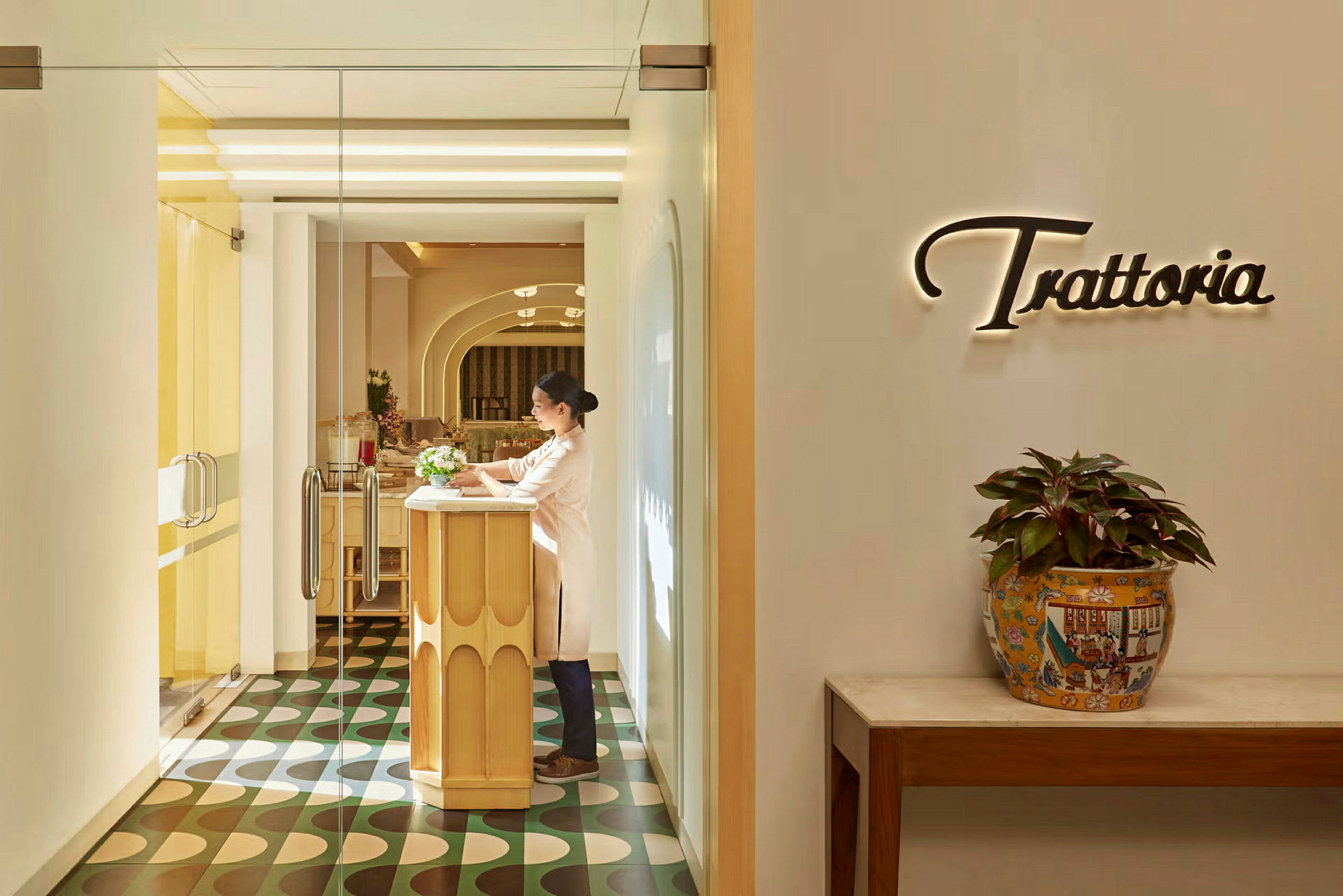 Inngangen til en restaurant med ordet 'Trattoria' på veggen og et bord med plante i potte. (AI-generert tekst)
