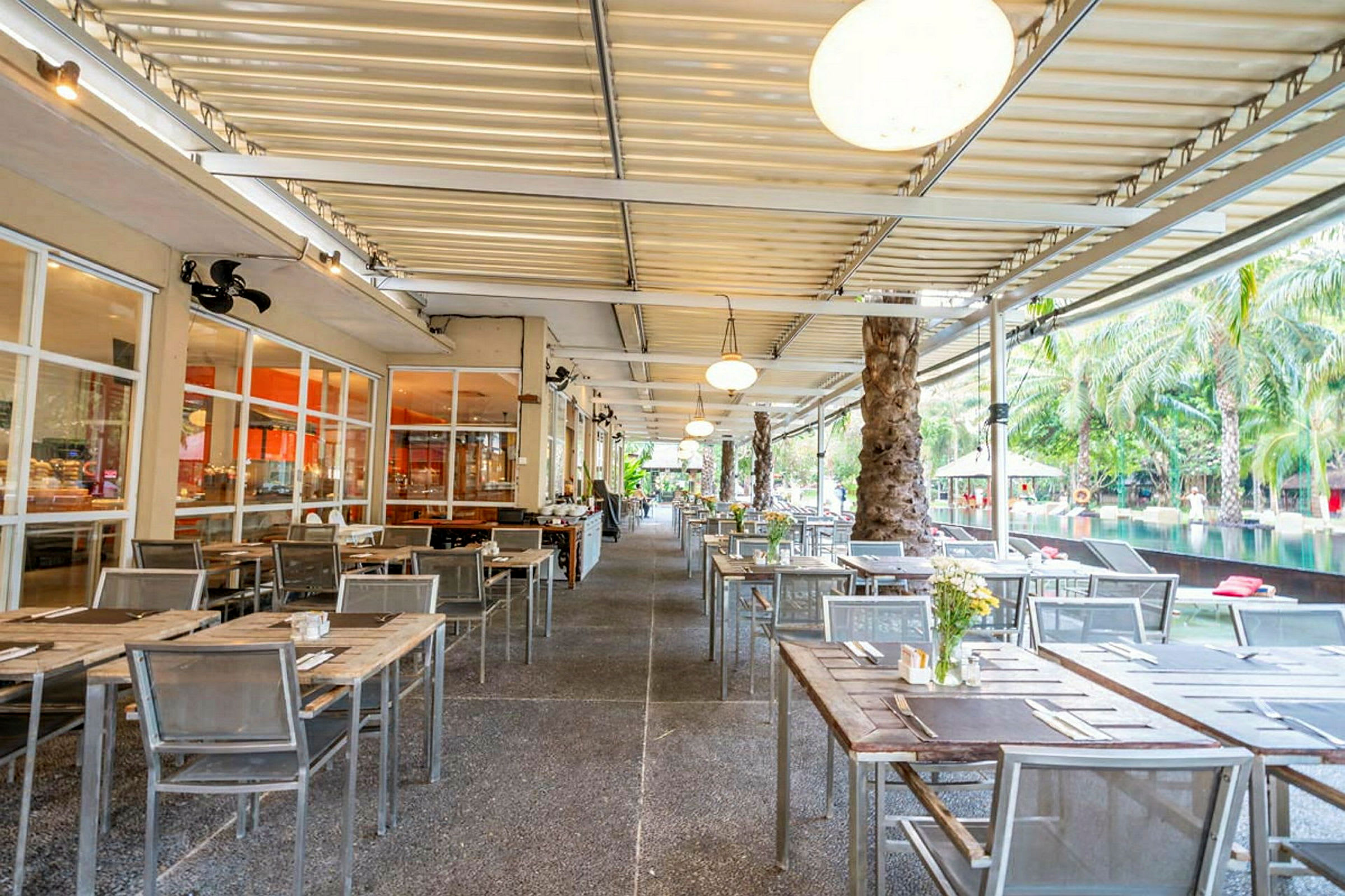 En utendørsrestaurant med bord og stoler arrangert under et overdekket tak. (AI-generert tekst)