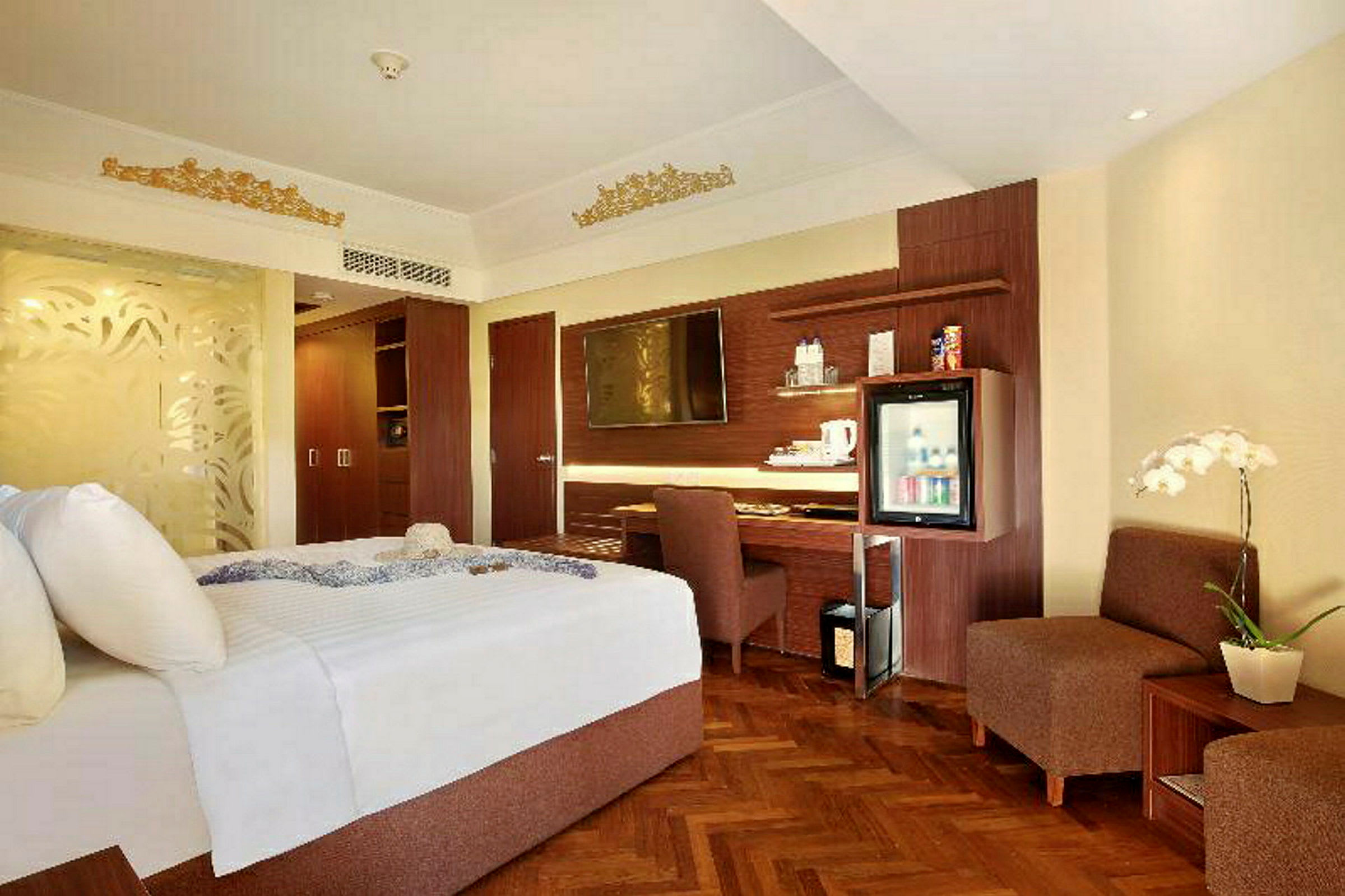 Et hotellrom med en stor seng, en skrivebordshjørne, en TV montert på veggen og en minibar. Innredningen er i lyse farger med innslag av tre. (AI-generert tekst)