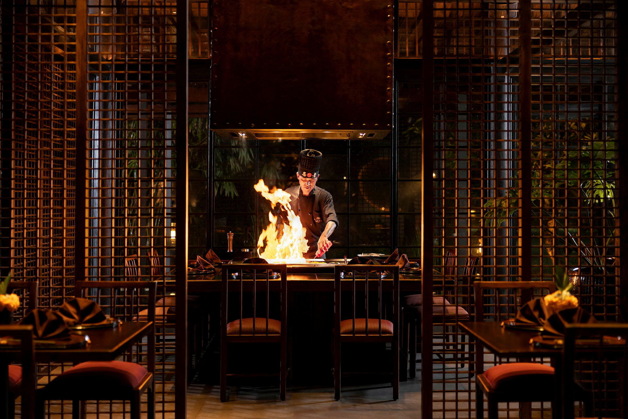 En restaurant med en kokk som tilbereder mat ved et bord foran flammer. (AI-generert tekst)