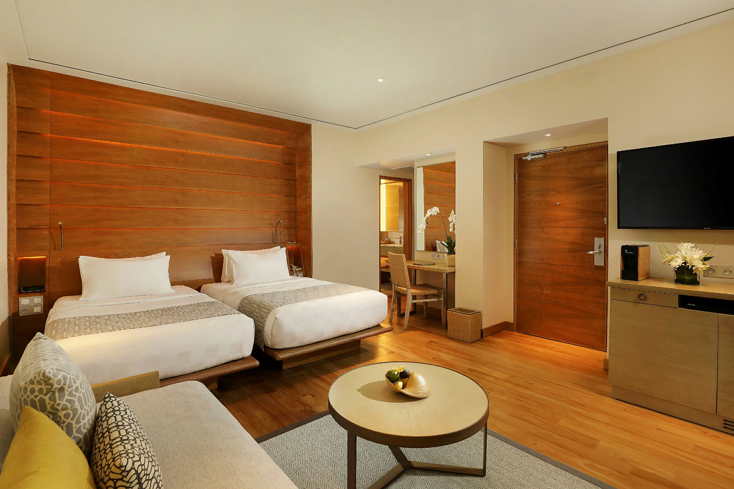 Et moderne hotellrom med to separate senger, et skrivebord med speil, en sofa og et lite bord. (AI-generert tekst)