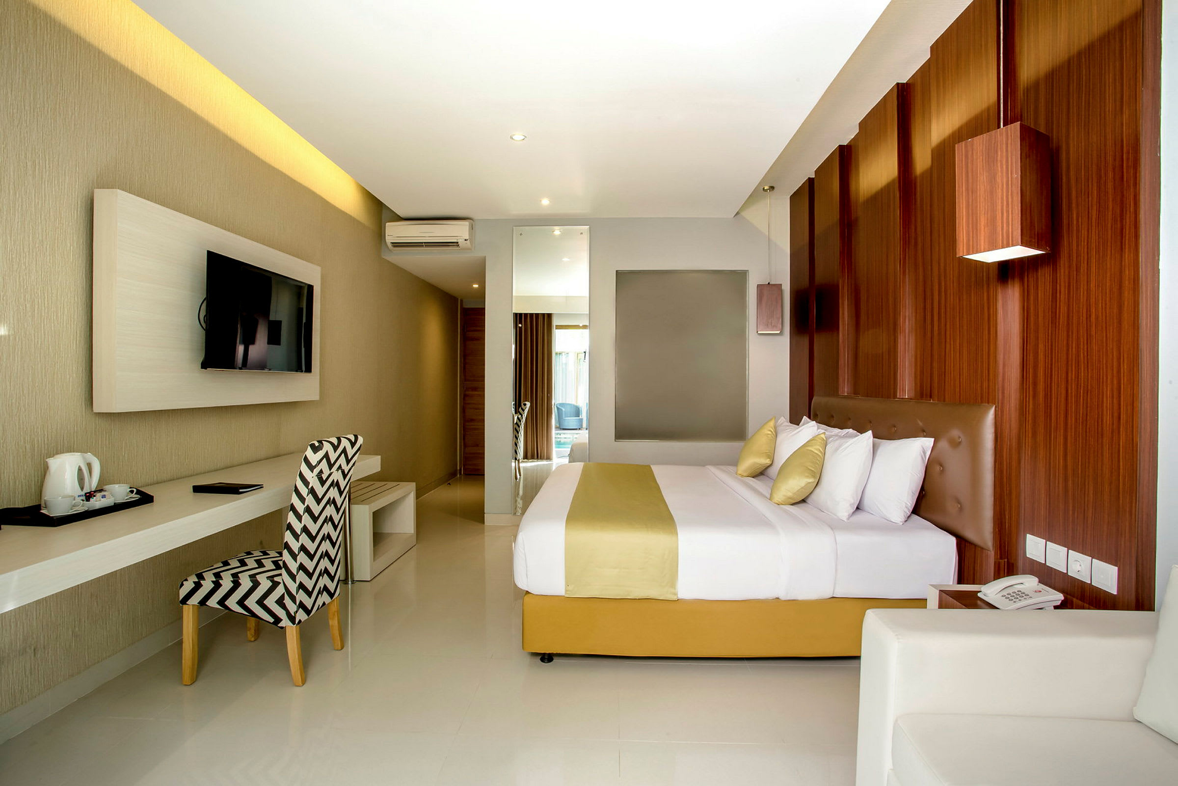 Et moderne hotellrom med en dobbeltseng, et skrivebord og en veggmontert TV. Innredningen er elegant med trepanel og lyse farger. (AI-generert tekst)