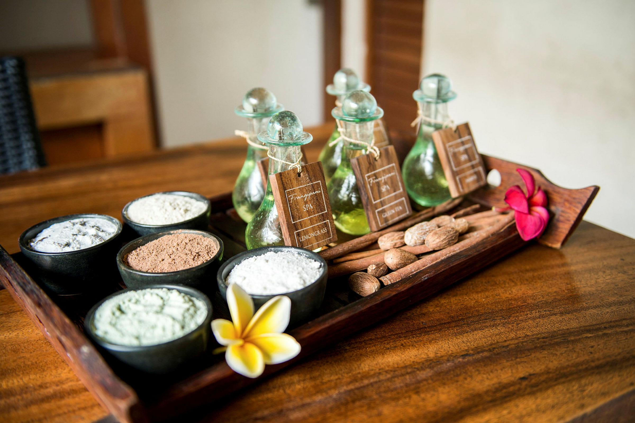 Et trebord med små skåler som inneholder ulike pulver og ingredienser samt små glassflasker med oljer. Det er også blomster og nøtter som dekorasjon. (AI-generert tekst)