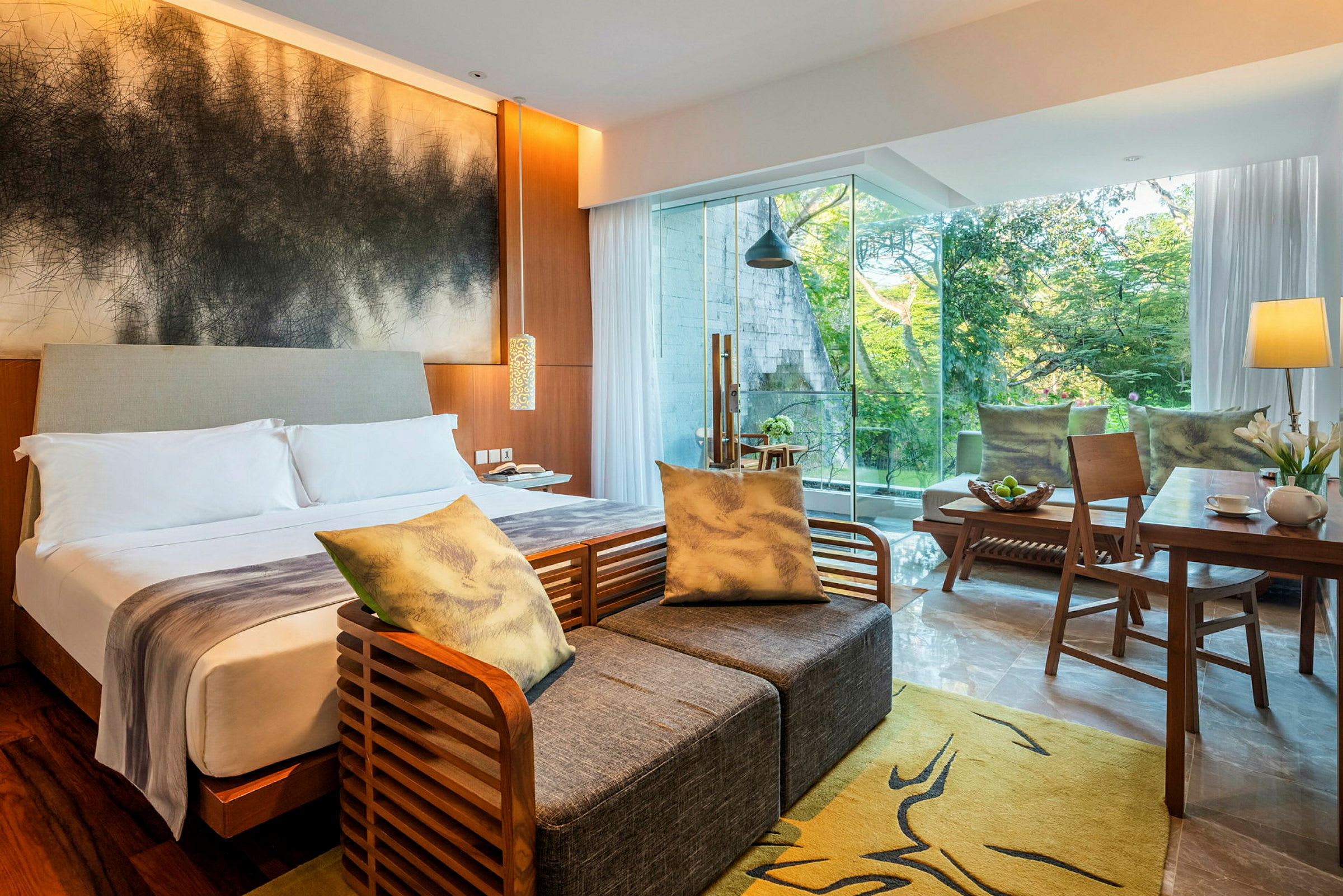 Et moderne hotellrom med en dobbeltseng, sittemøbler, et skrivebord og store vinduer som viser grønt utenfor. (AI-generert tekst)