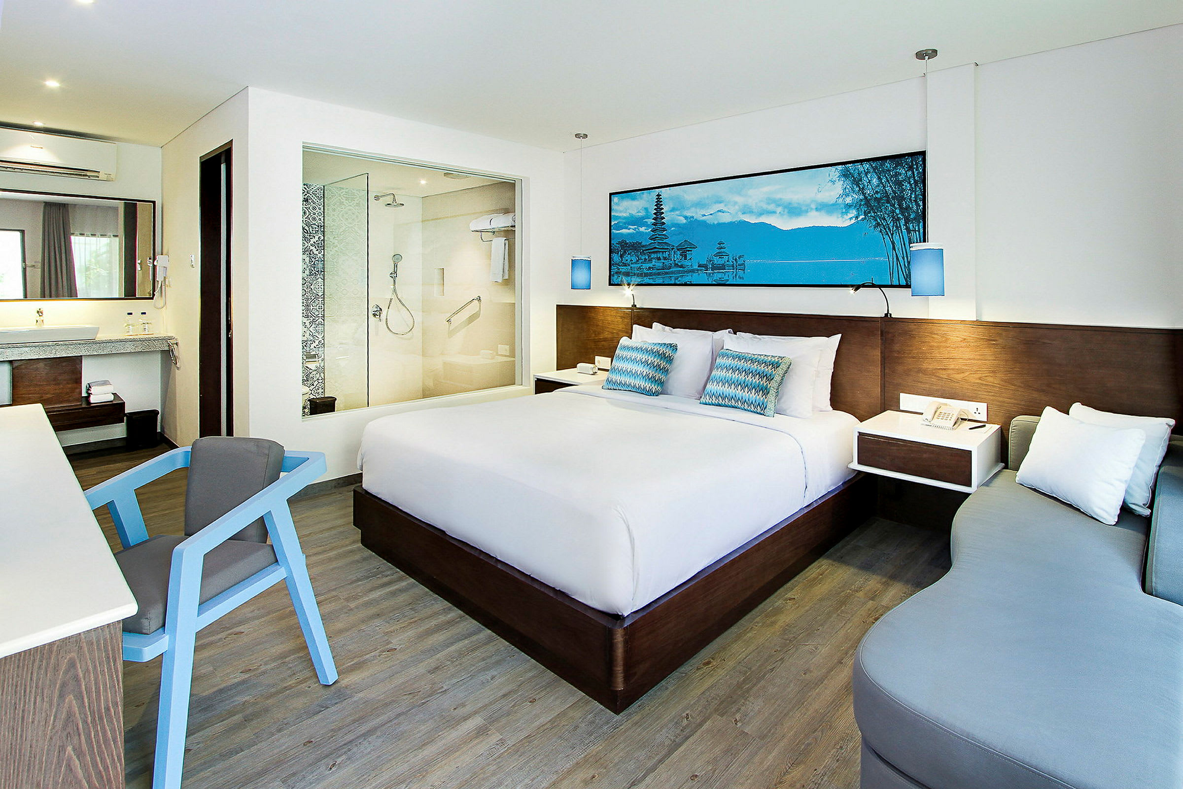 Et moderne hotellrom med en stor seng, et skrivebord med en stol, en sofa og et baderom med glassvegg. (AI-generert tekst)