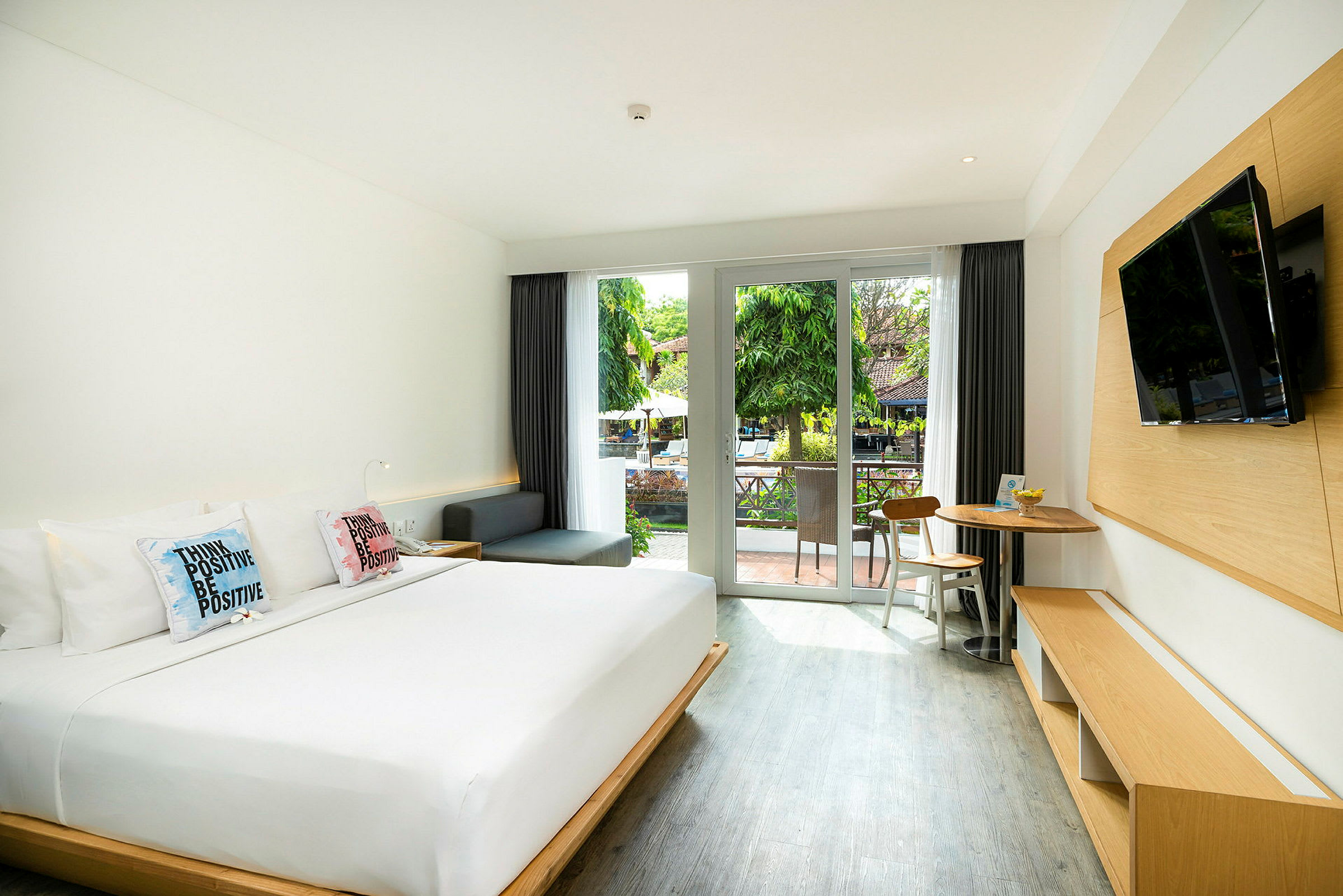 Hotellrom med en stor seng, en sittegruppe og en balkong med utsikt over en grønn hage. (AI-generert tekst)