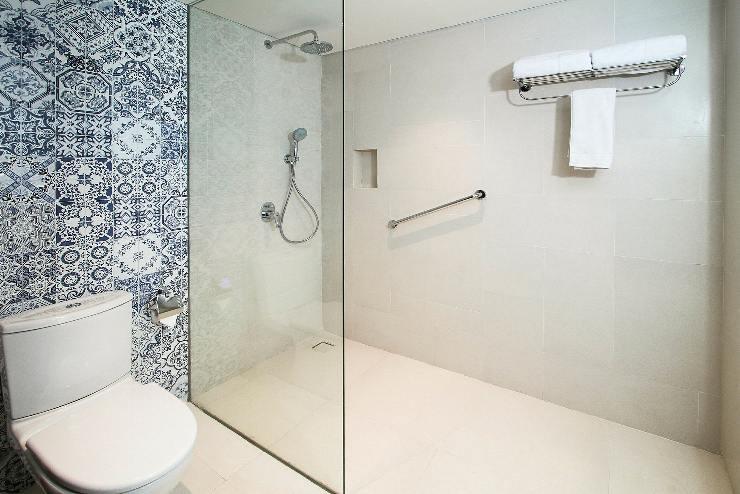Bad med moderne design, dusjområde med glassvegg og flisvegg med blå-hvite mønstre. Toalett ved siden av. (AI-generert tekst)