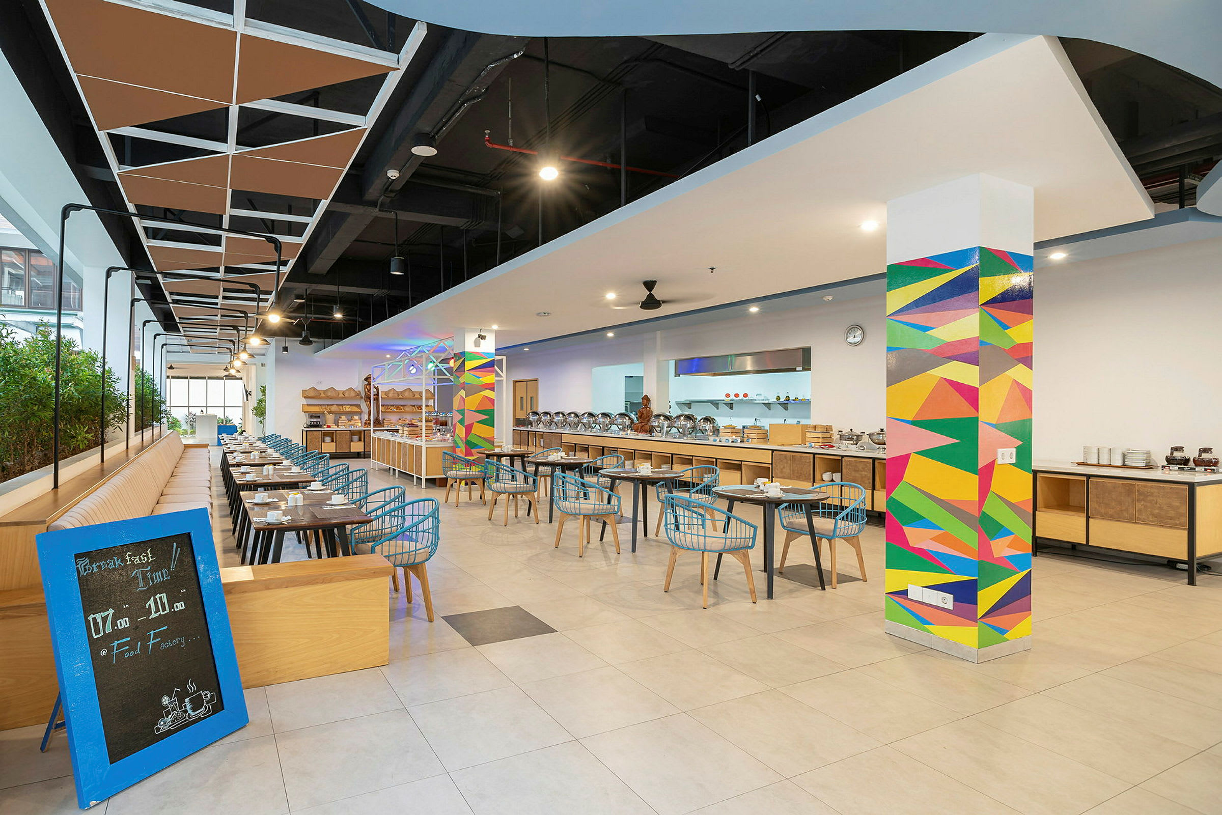 Interiør av en moderne restaurant med fargerike veggdekorasjoner og sitteplasser arrangert langs bord. (AI-generert tekst)