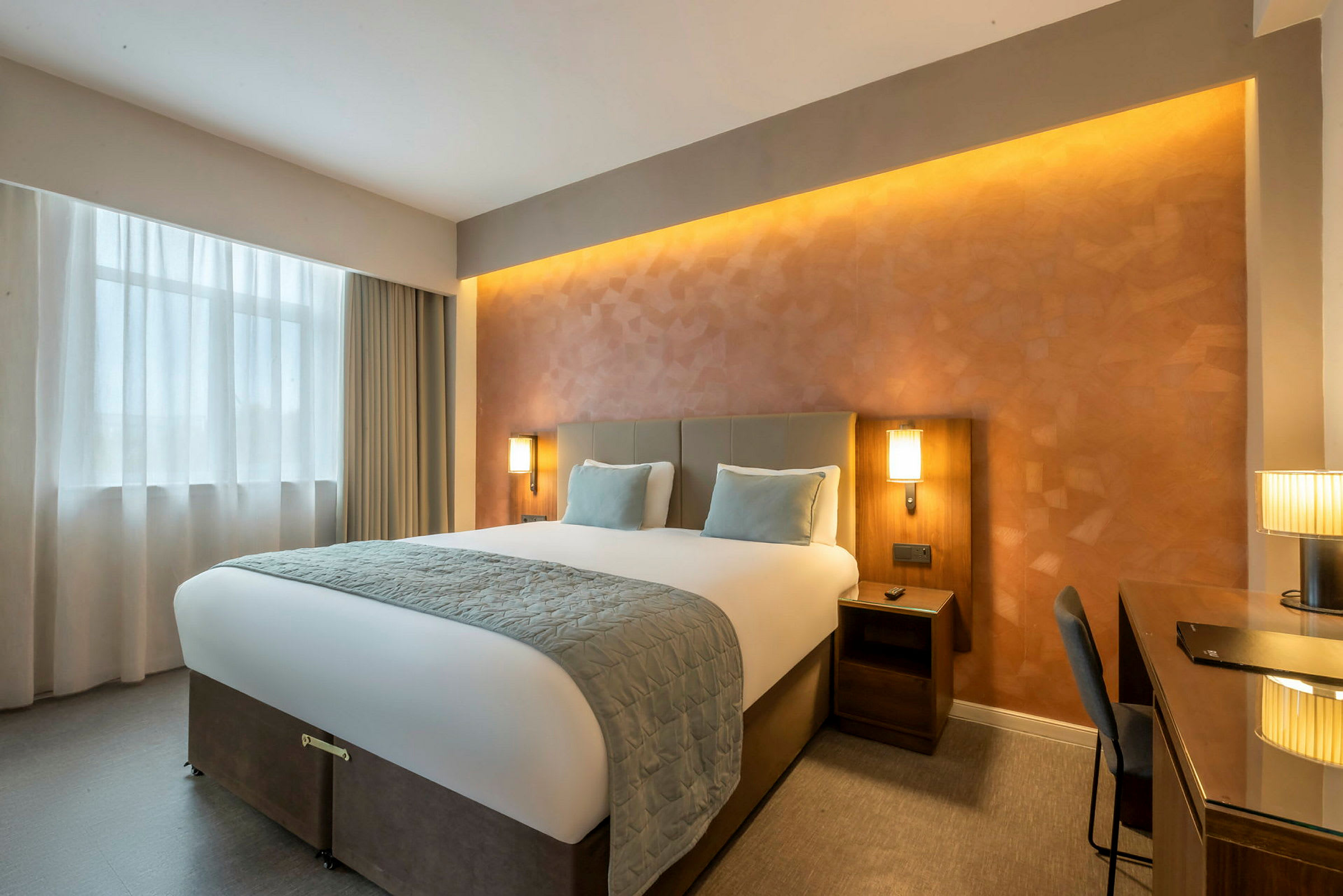 Et hotellrom med en stor seng, to nattbord og et skrivebord. (AI-generert tekst)