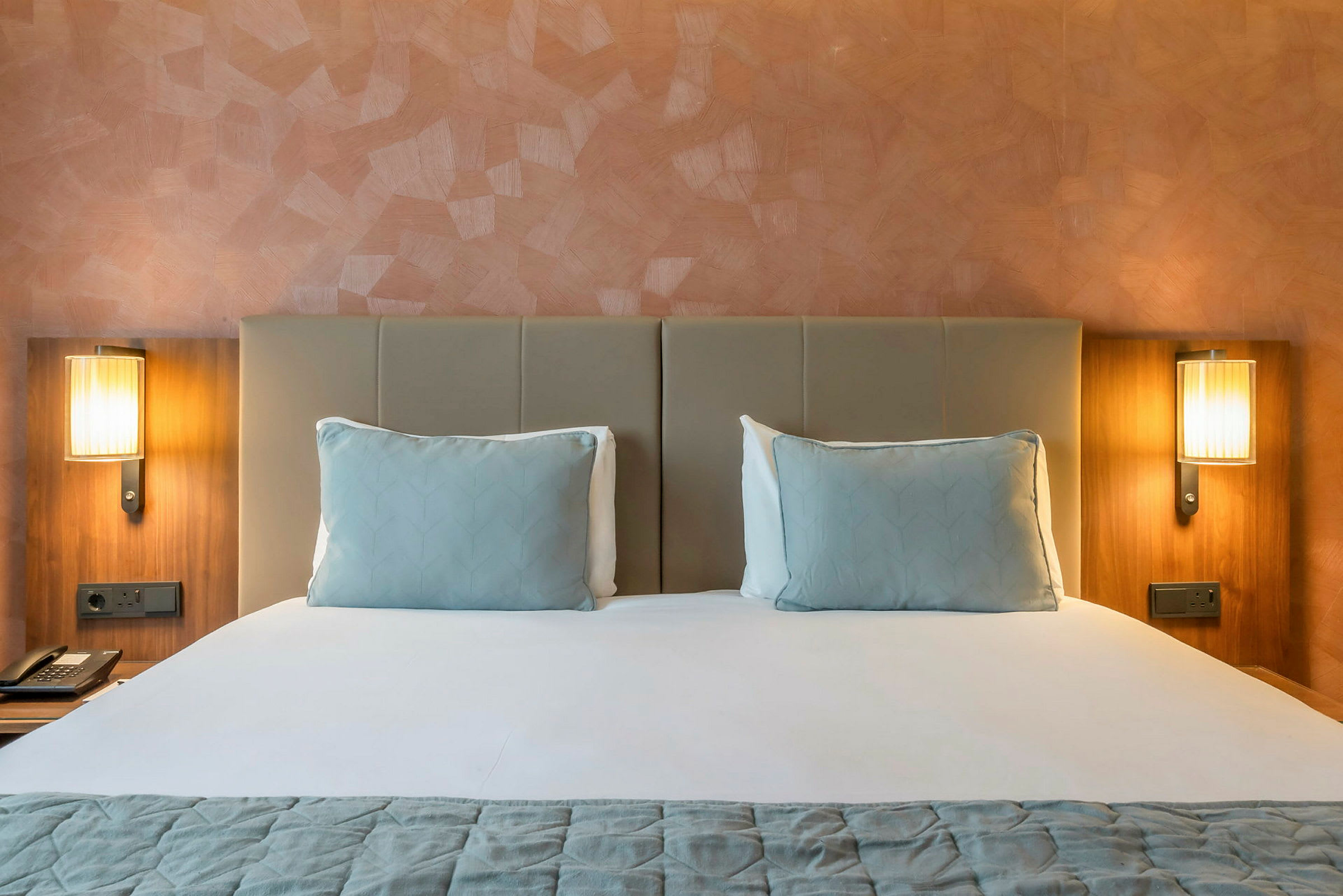 Hotellseng med to puter og to nattbordslamper. (AI-generert tekst)