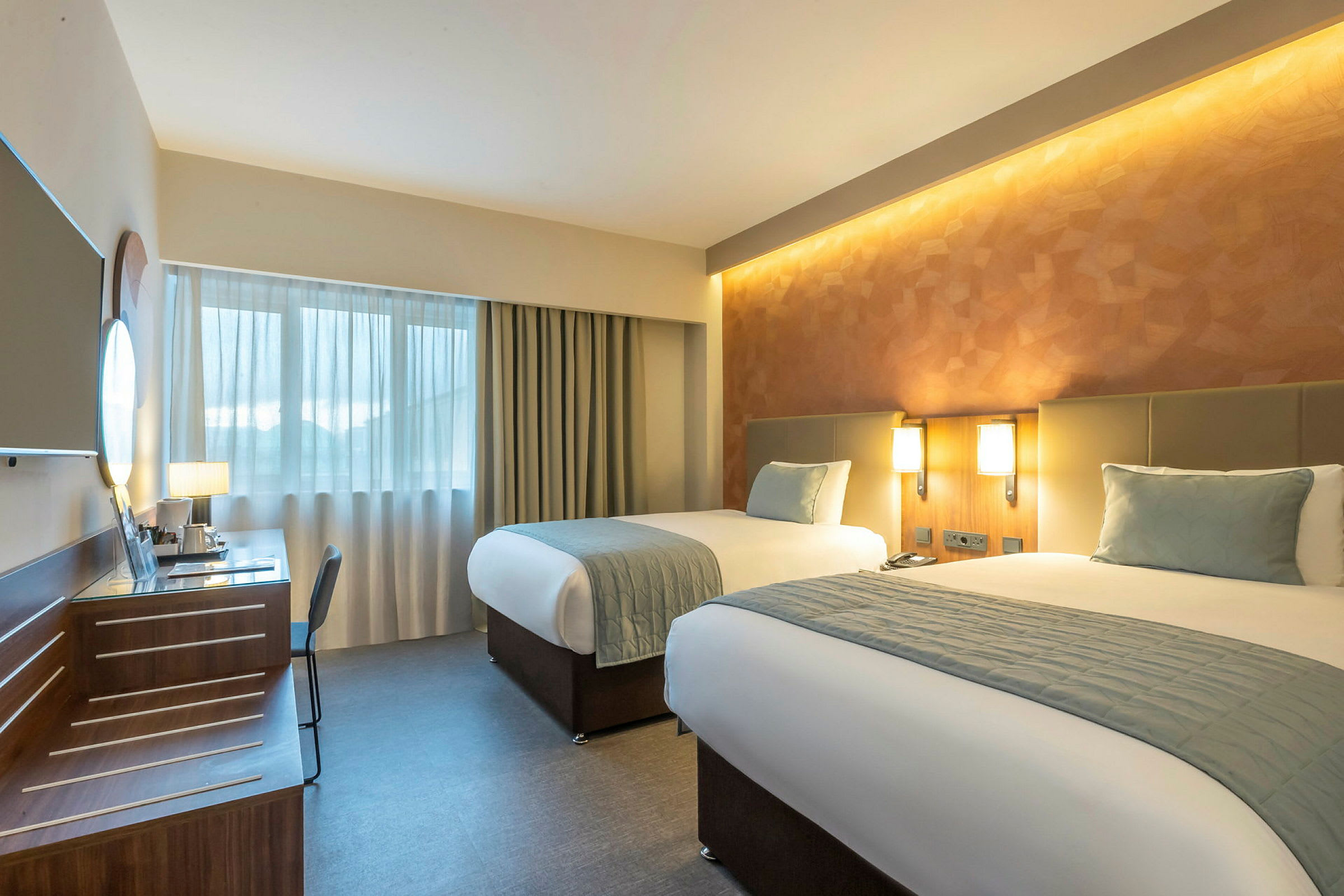 Et hotellrom med to enkeltsenger, skrivebord og vindu. (AI-generert tekst)