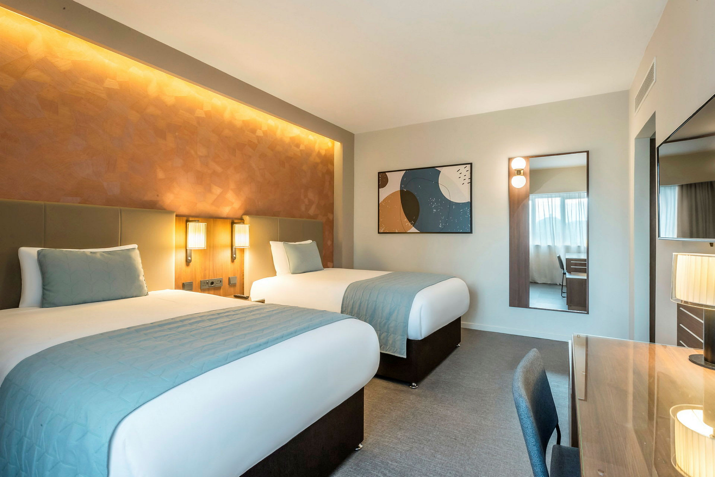 Hotellrom med to enkeltsenger, skrivebord og speil. (AI-generert tekst)