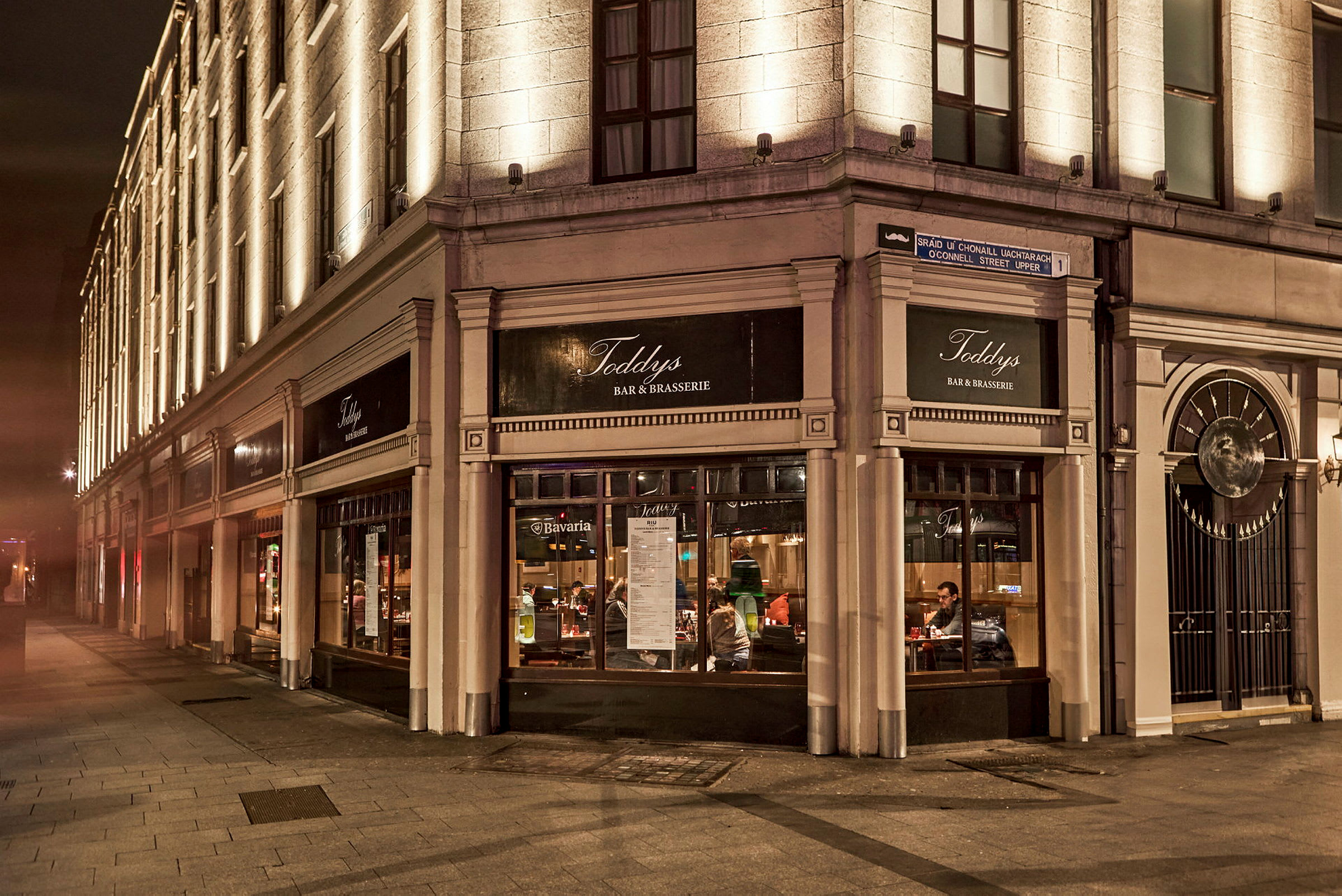 En steinbygning med opplyste fasader og en restaurant merket med skilt som viser Toddy's Bar & Brasserie. (AI-generert tekst)