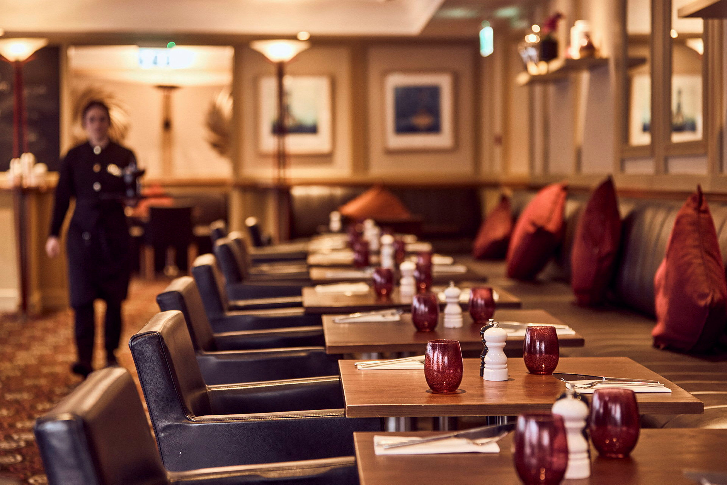 En restaurant med dekkede bord, røde glass og mørke stoler vises på bildet. (AI-generert tekst)