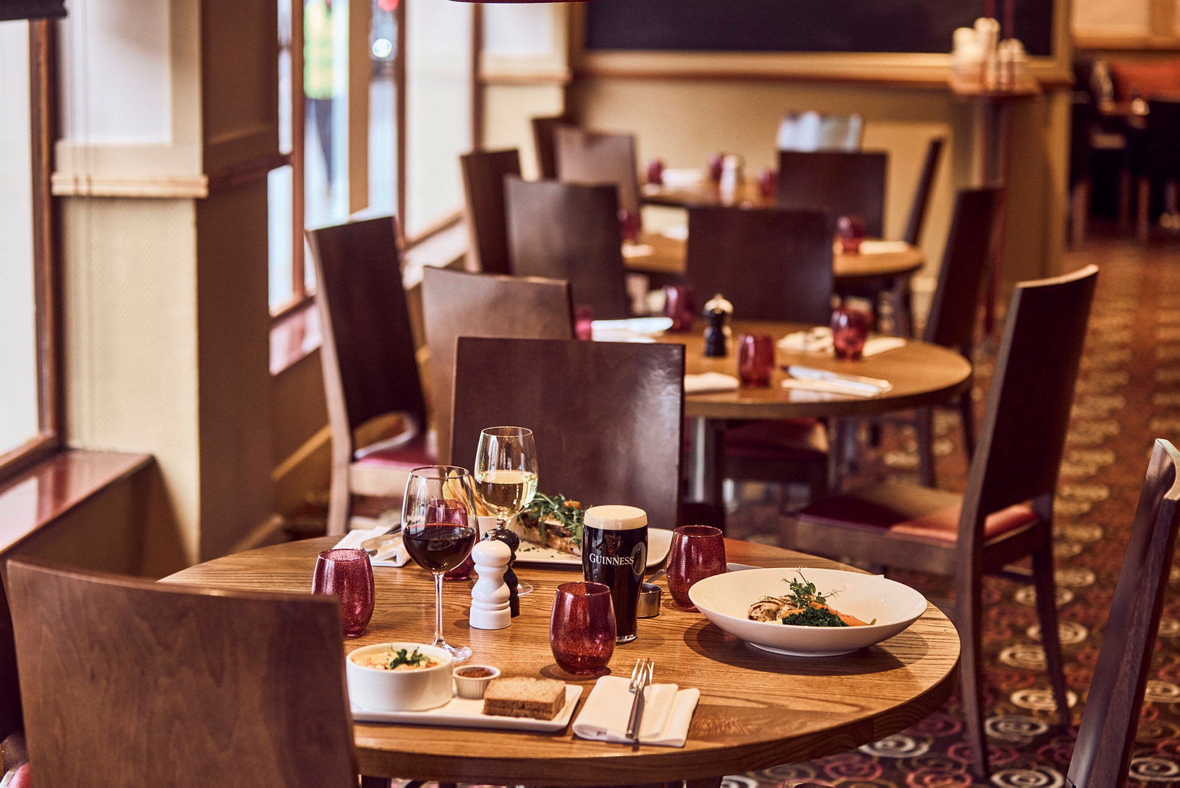 Et restaurantbord med to vinglass og servert mat på tallerkener. (AI-generert tekst)