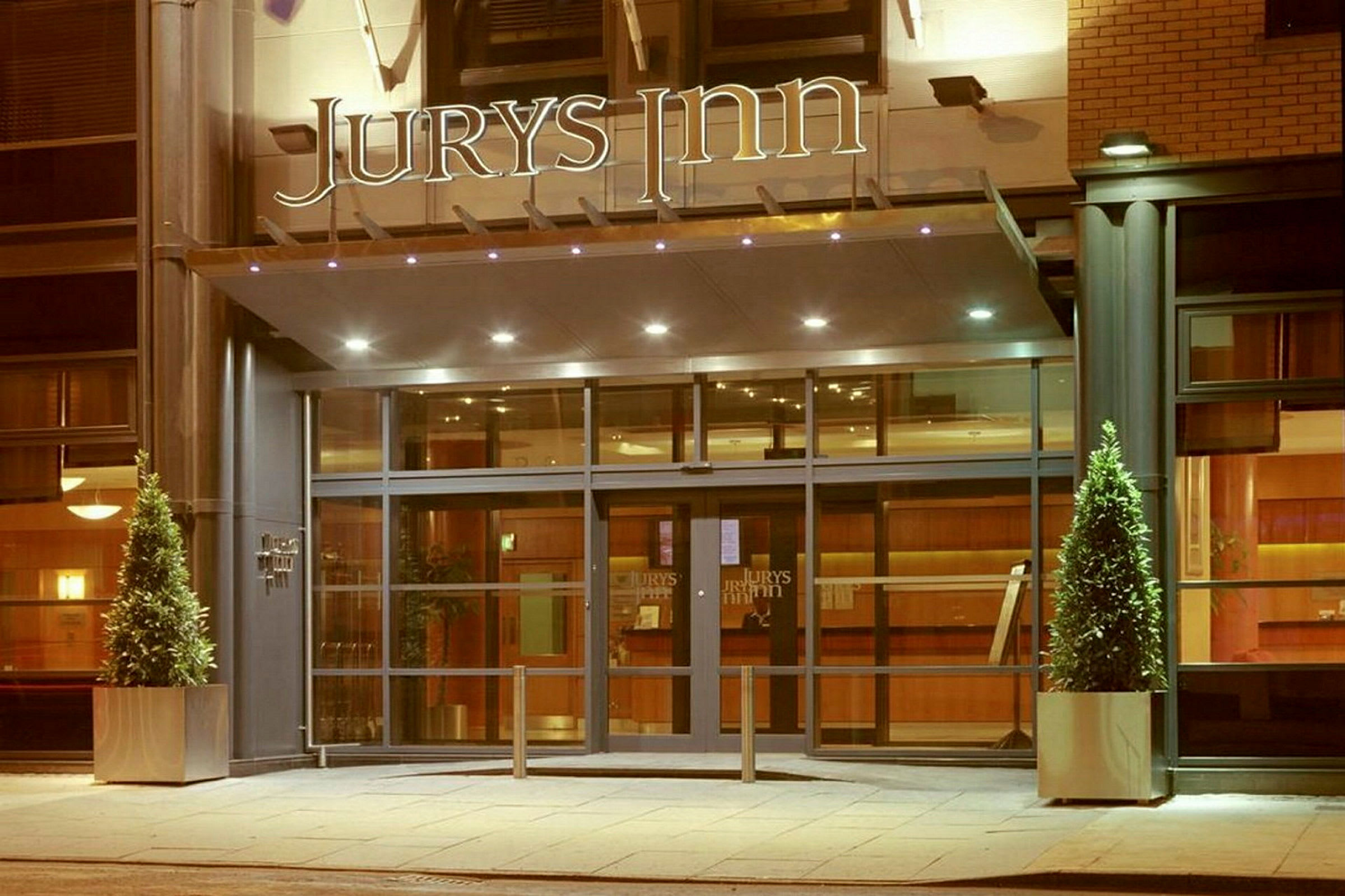 Hotellinngang med glassdører og skiltet 'Jurys Inn' over. (AI-generert tekst)