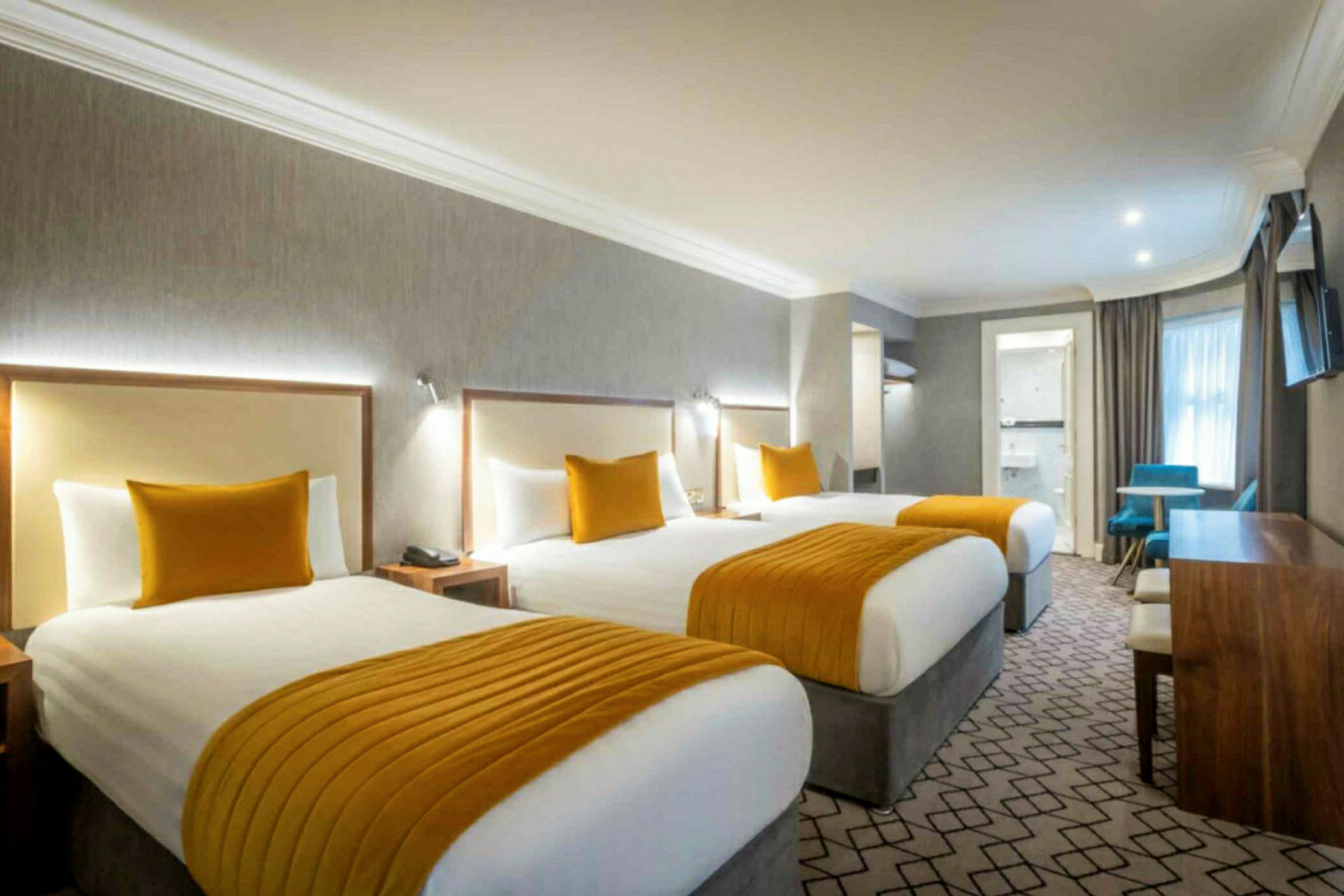 Hotellrom med tre senger, oransje detaljer og skrivebord. (AI-generert tekst)